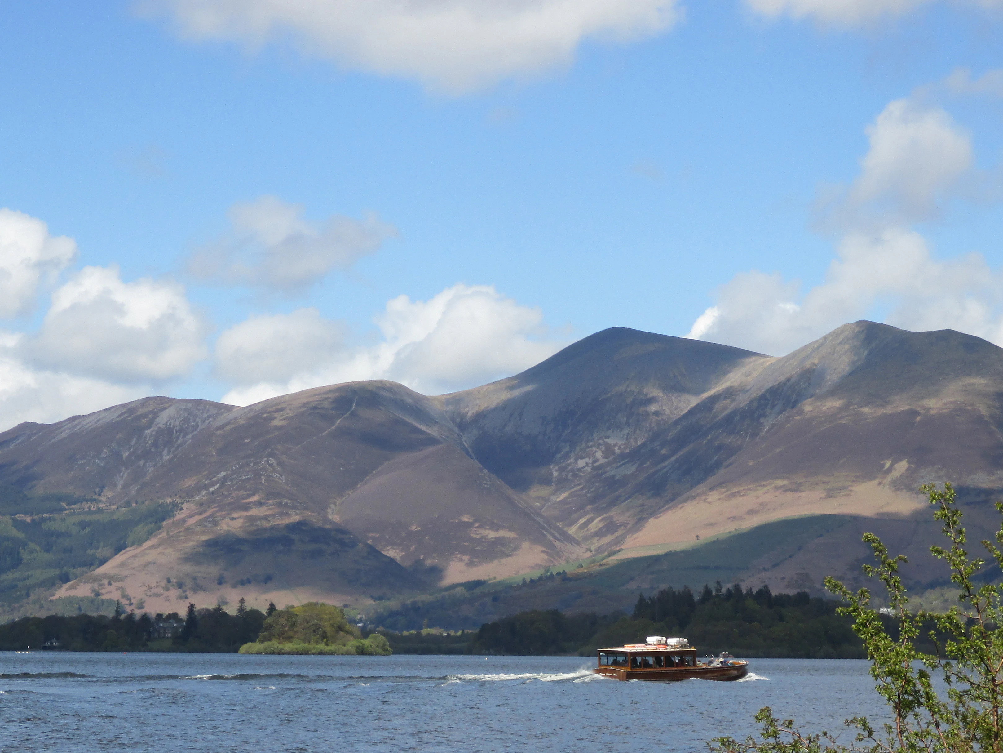 A lake with a passenger ferry boat, mountains in the background under a partly cloudy sky