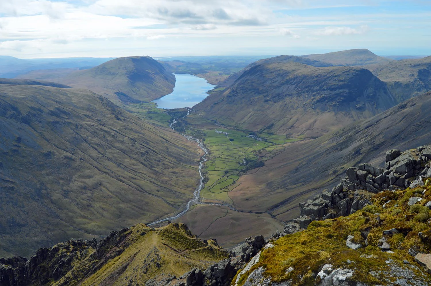 Panoramic mountain landscape view with a lake, river, and valleys under a partly cloudy sky
