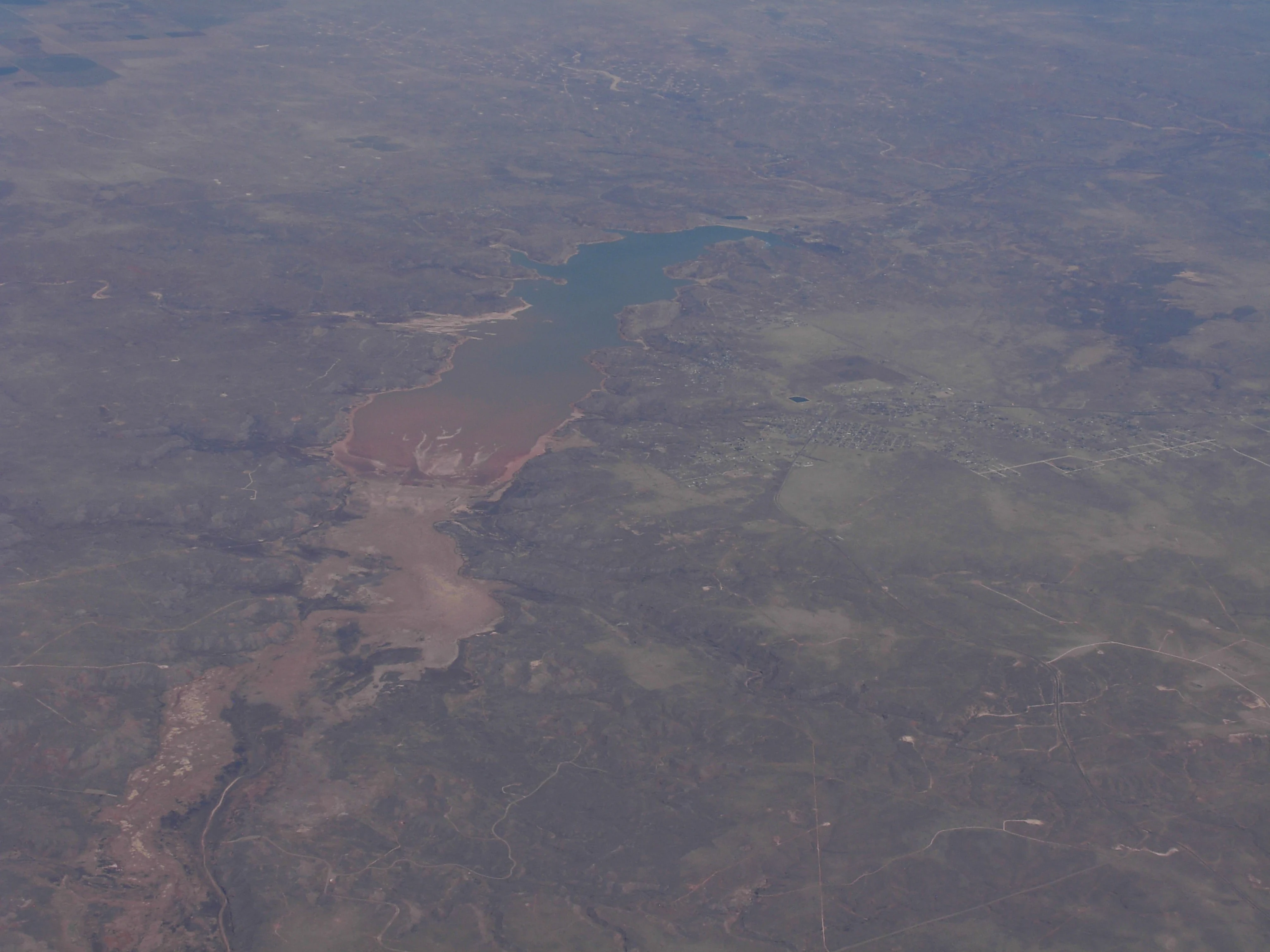 An aerial perspective of a reservoir surrounded by arid, sparsely vegetated terrain.