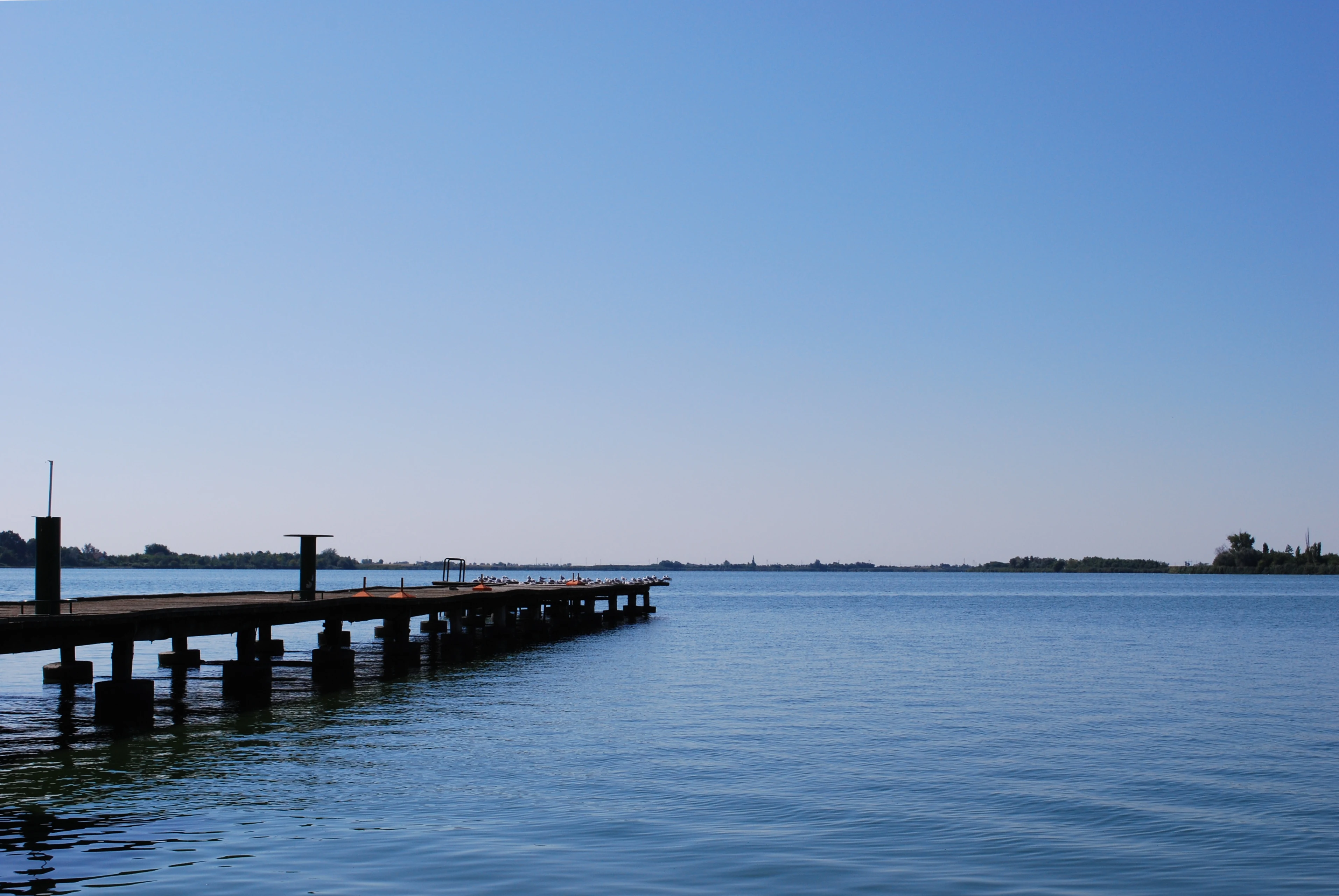 Calm lake with a wooden pier extending into the water under a clear blue sky