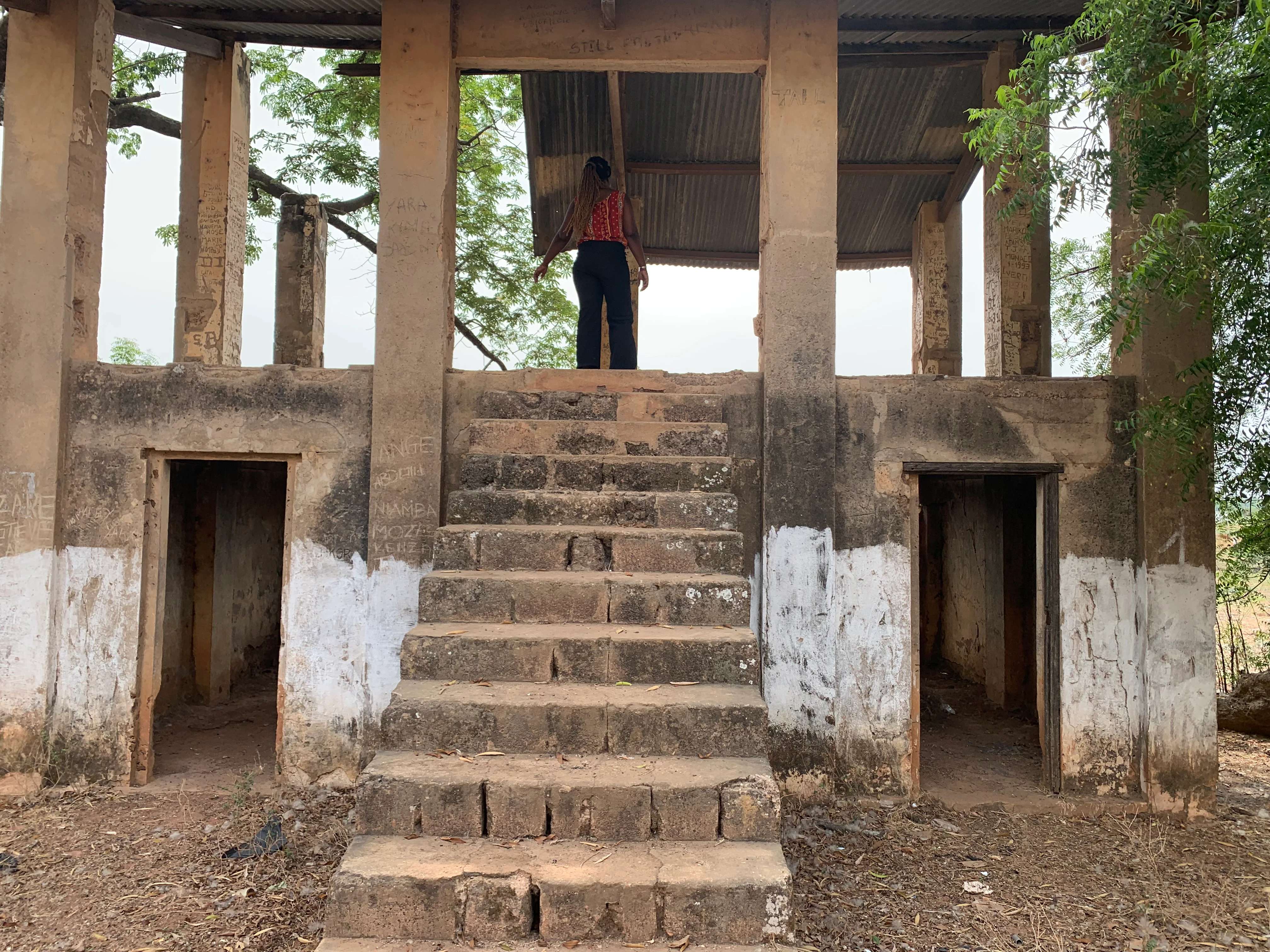 A weathered, multi-level concrete structure with a central stone staircase leading to an open upper deck, where a person stands looking out.