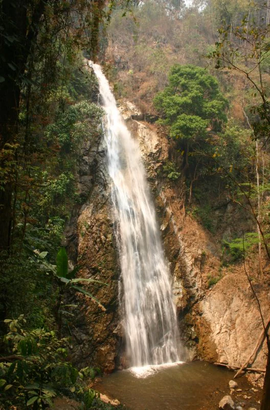 A tall waterfall cascading down rocky cliffs surrounded by dense green forest in a tropical setting