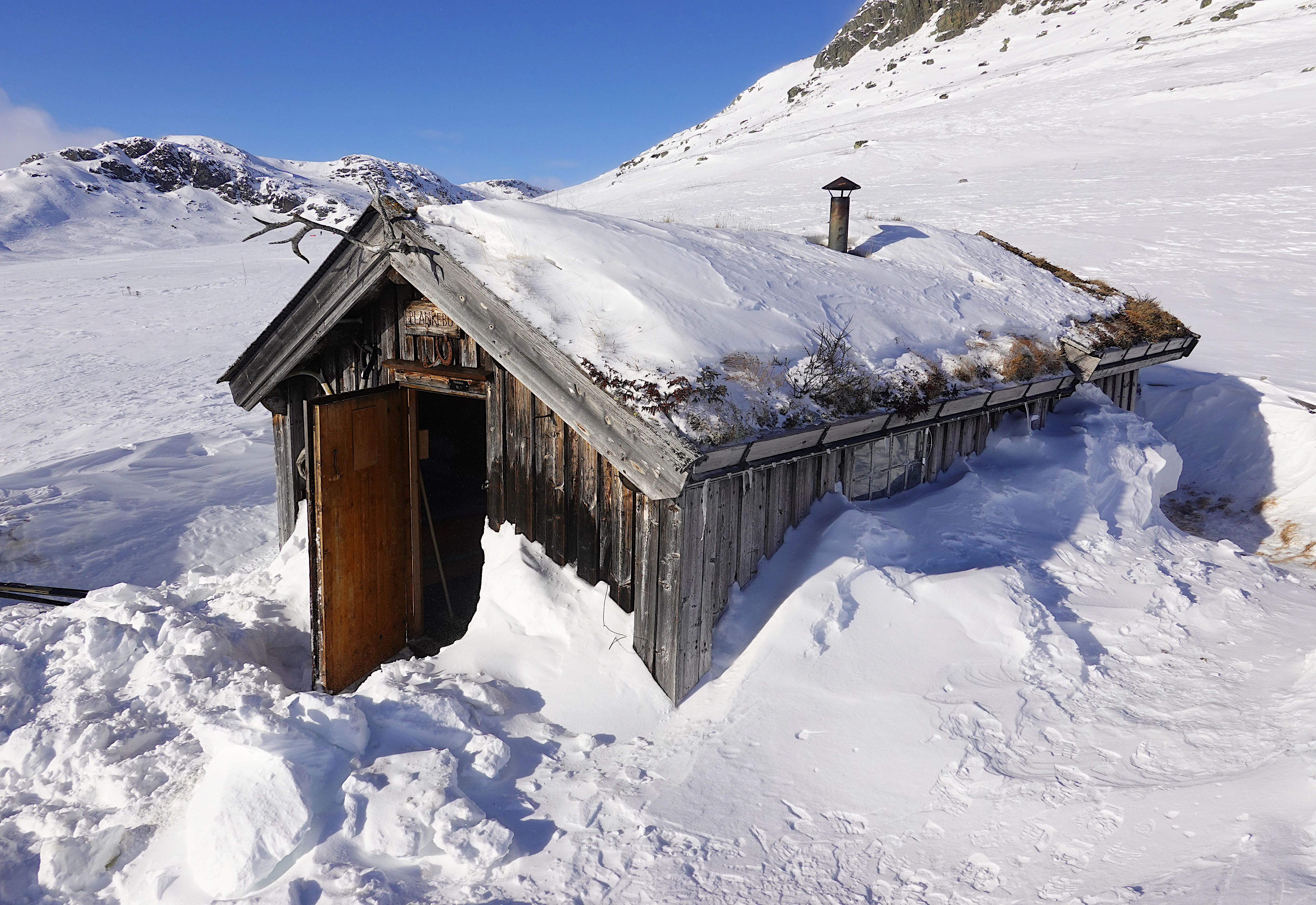 Wooden shelter with snow-covered roof surrounded by snow in a mountainous landscape