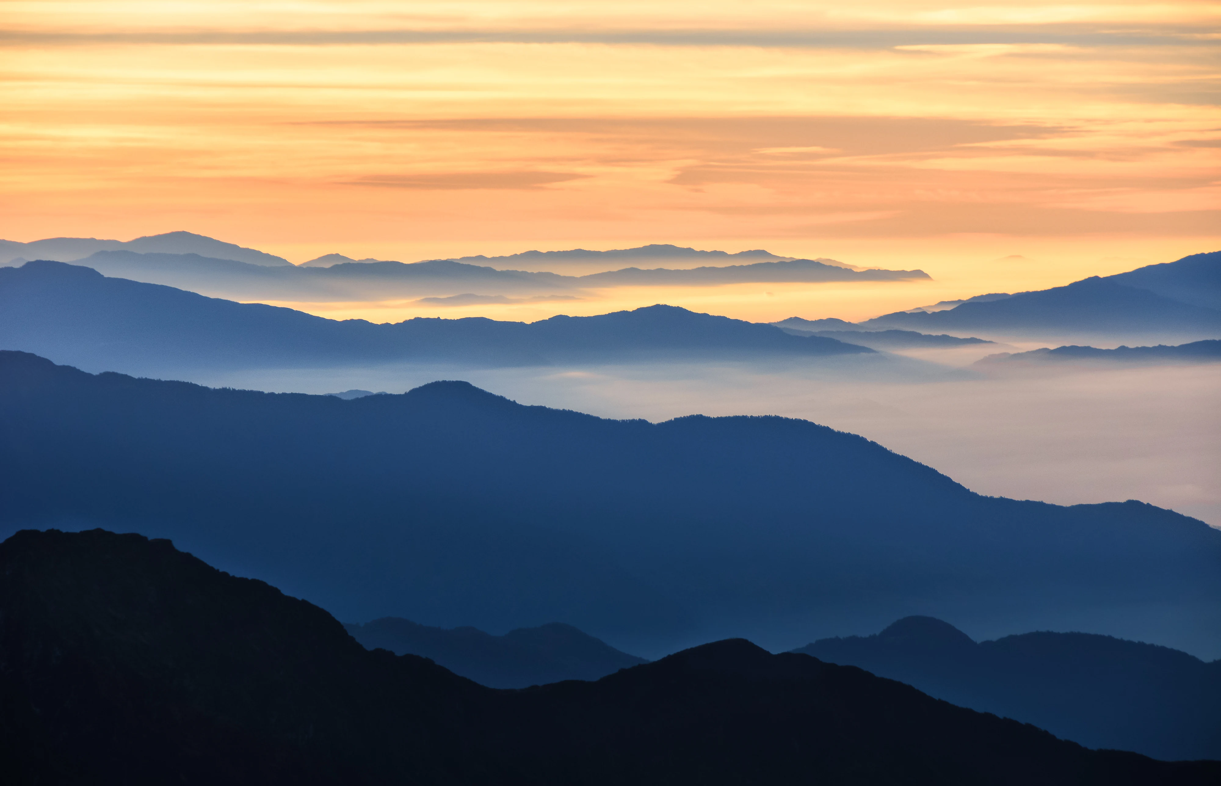 Silhouetted mountain ranges under a colorful sunrise sky with layered peaks and mist