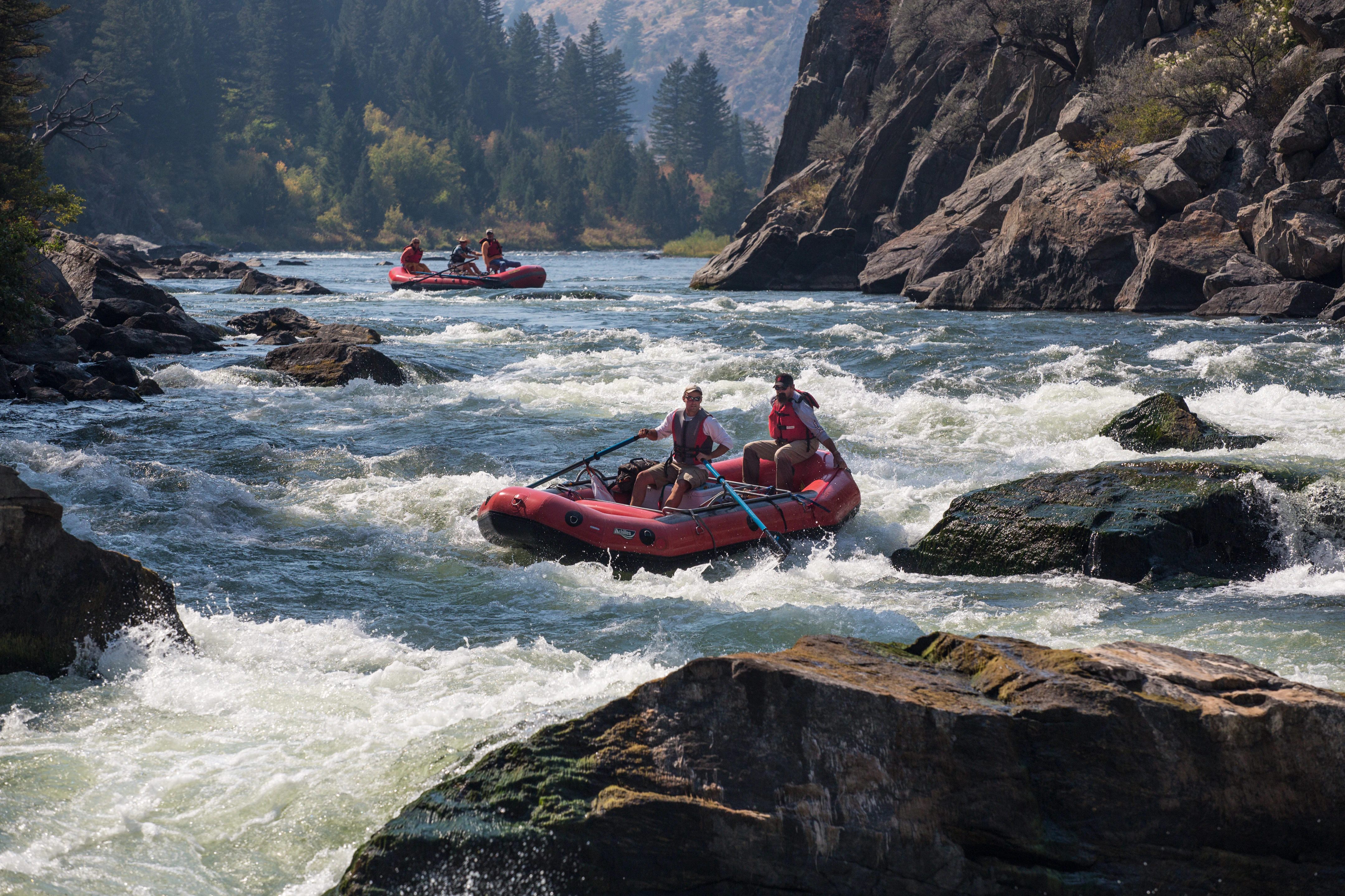Two red inflatable rafts navigating whitewater rapids between rocky canyon walls.