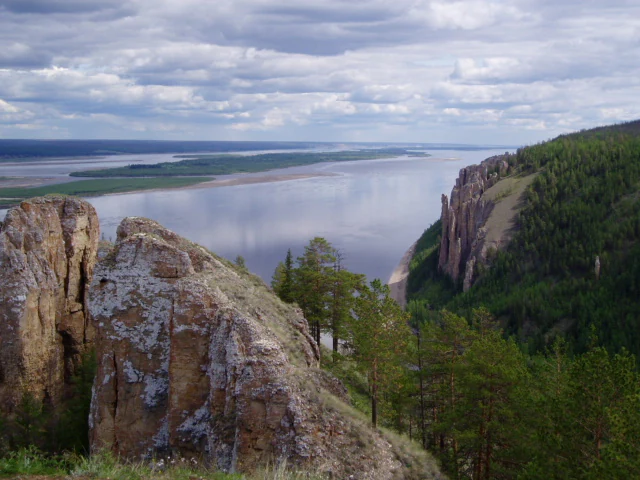 Wide landscape shot of the tall vertical rock formations of Lena Pillars overlooking a wide river under a cloudy sky.