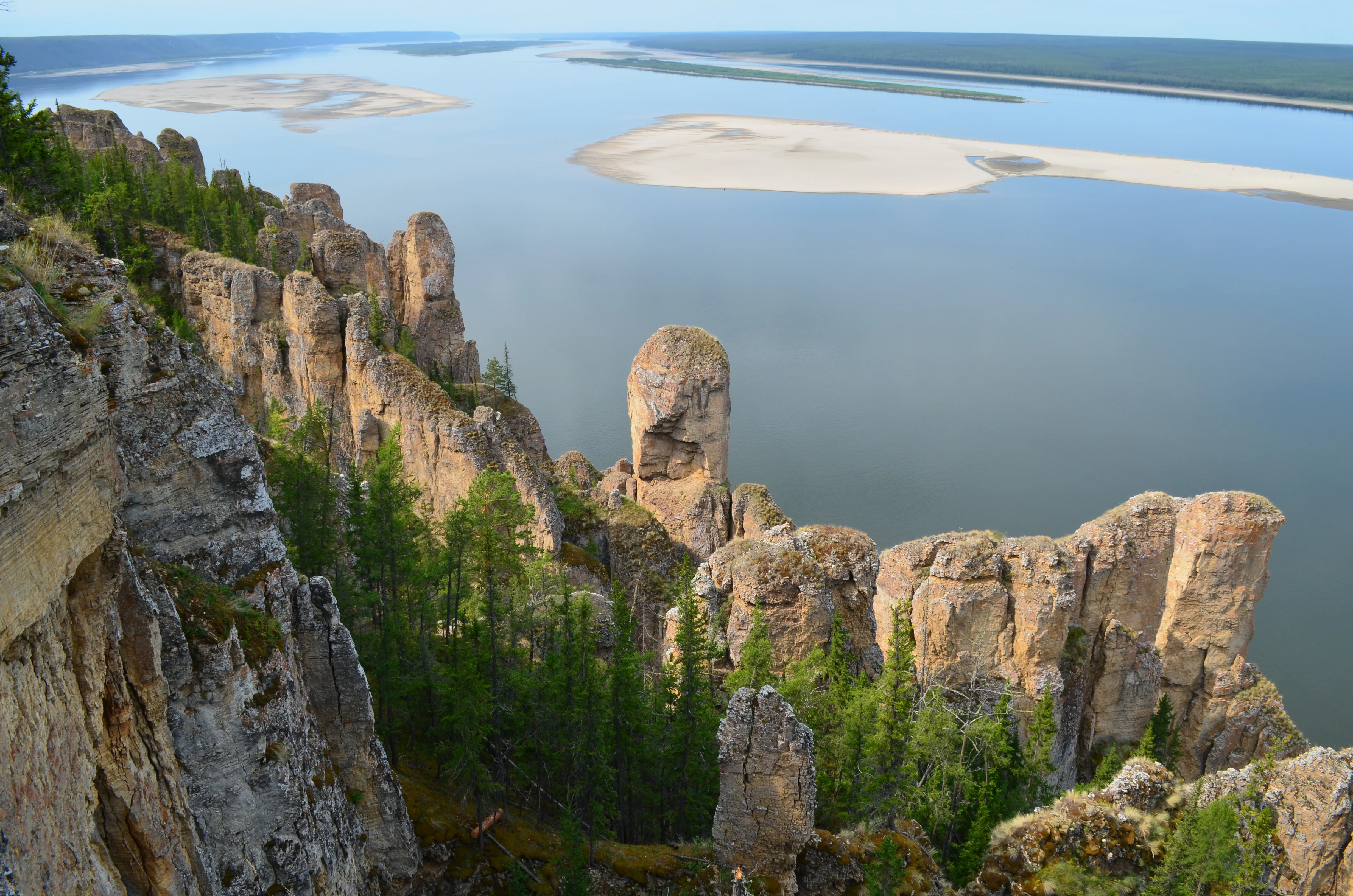 Rock pillars rising from forested riverbank, with Lena River and sandbars in the background