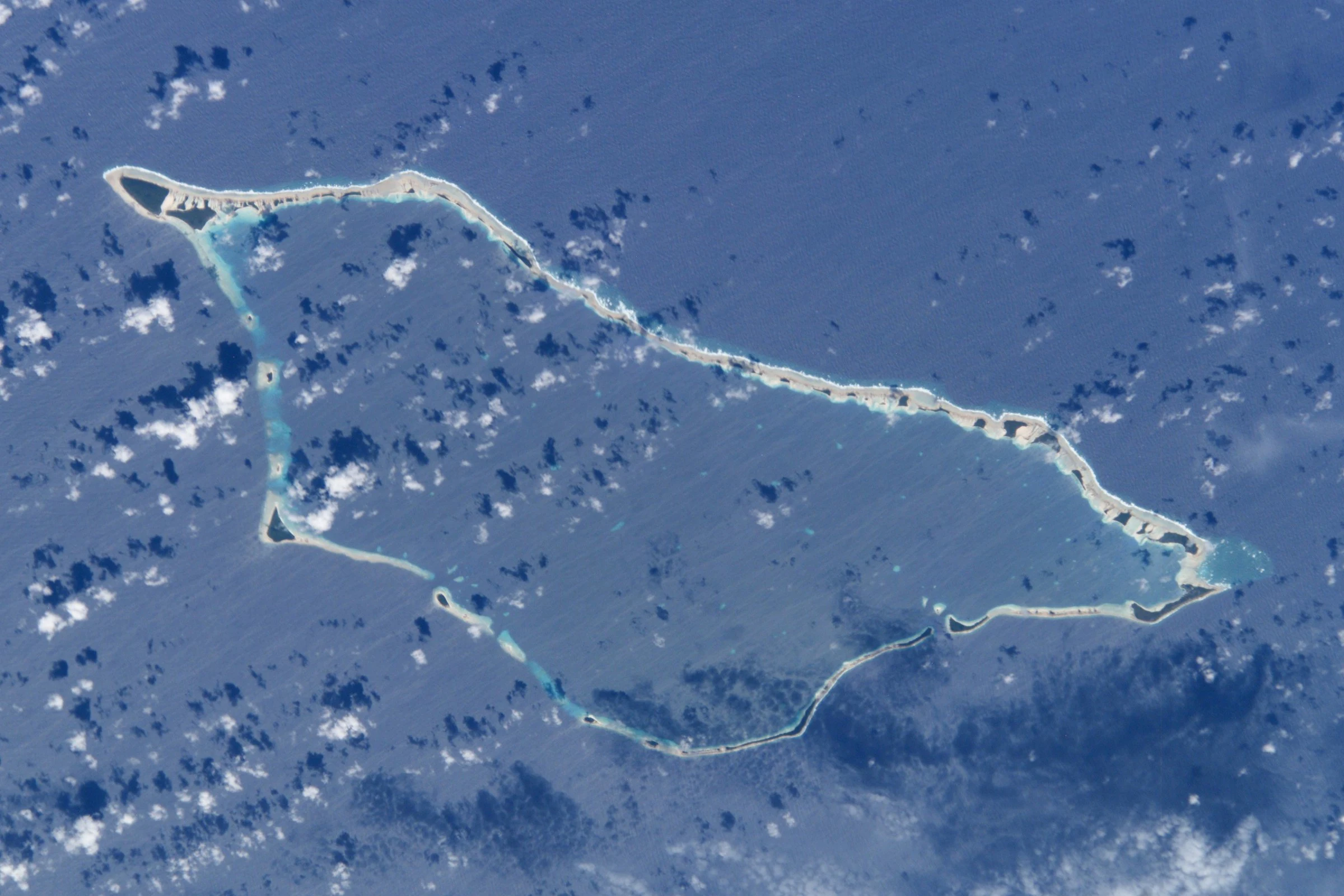 Aerial satellite image of Likiep Atoll, a ring-shaped coral atoll with a large central lagoon surrounded by deep blue ocean and scattered clouds.