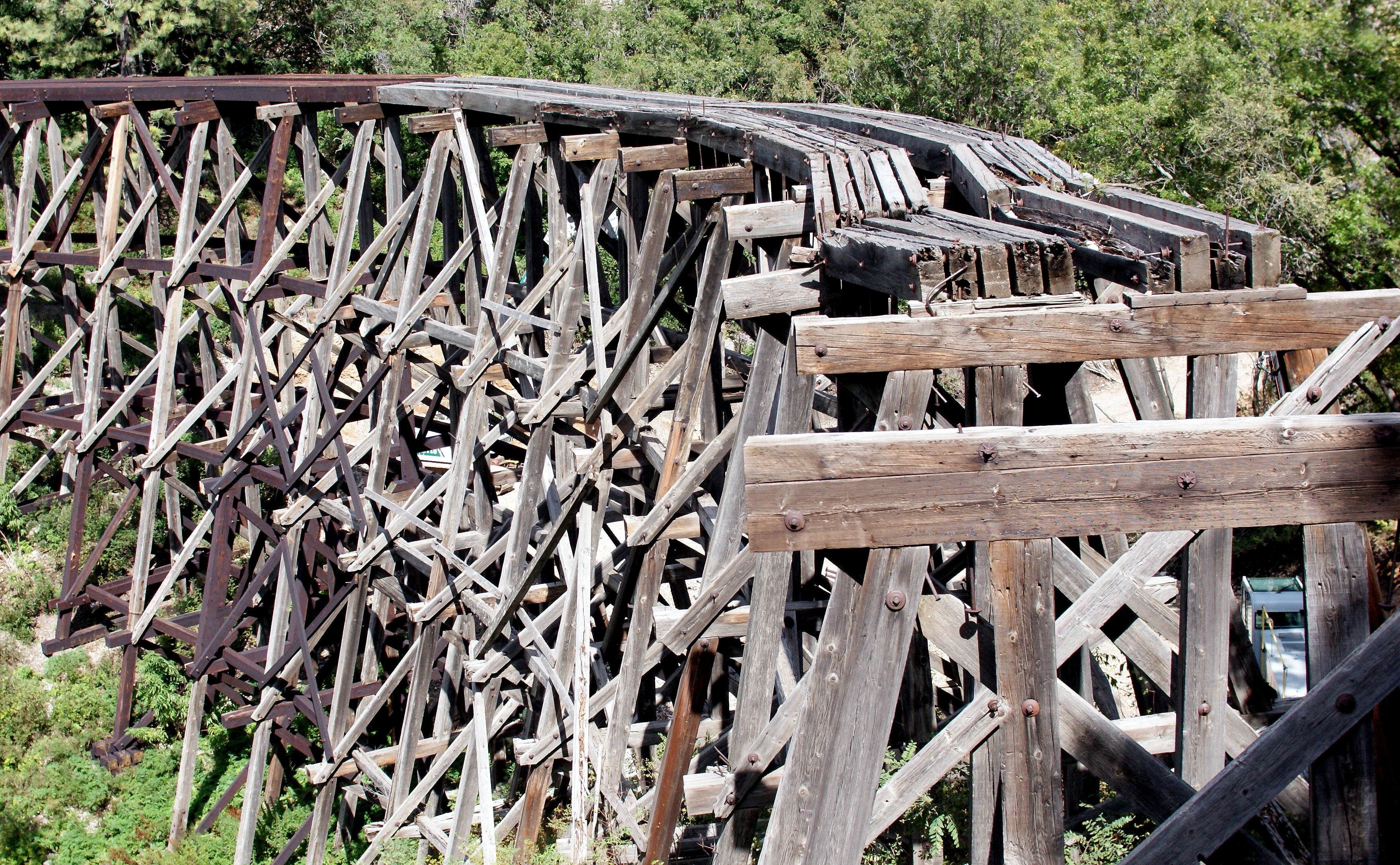 A close up view of the historic wooden Mexican Canyon Trestle railway bridge featuring a complex timber framework set against a backdrop of trees.