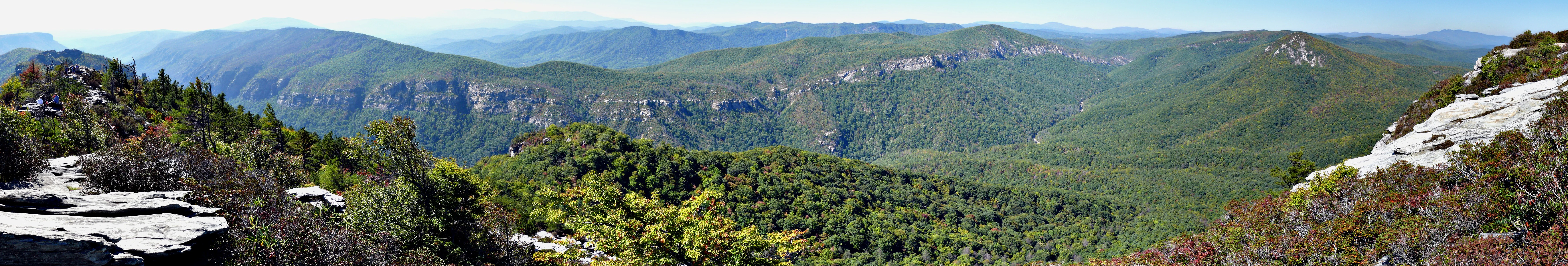 Wide panoramic landscape view from a high rocky vantage point looking over a dense forest covered canyon gorge with distant layered ridgelines.