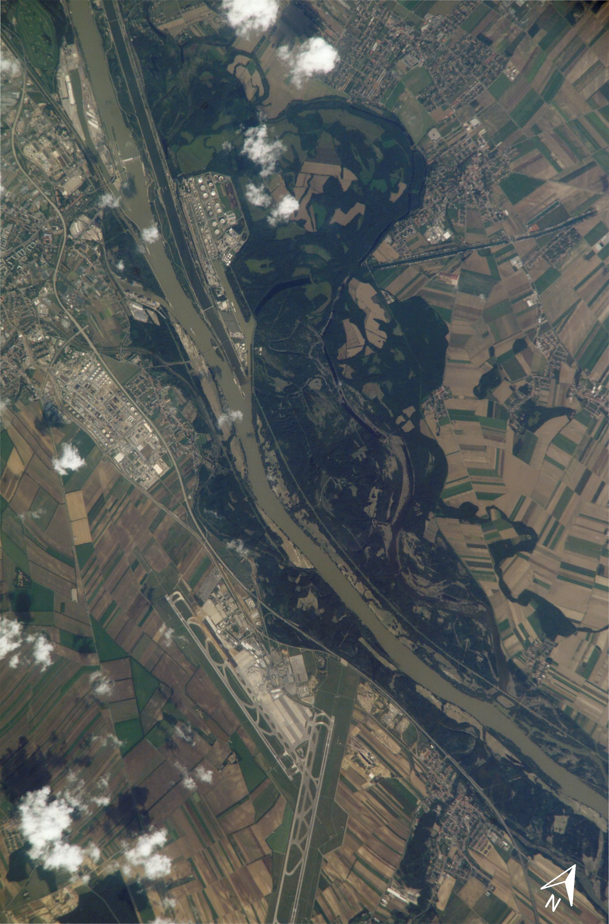Top-down satellite imagery showing the Danube river, the forested Lobau floodplain, and a large airport complex surrounded by agricultural fields.