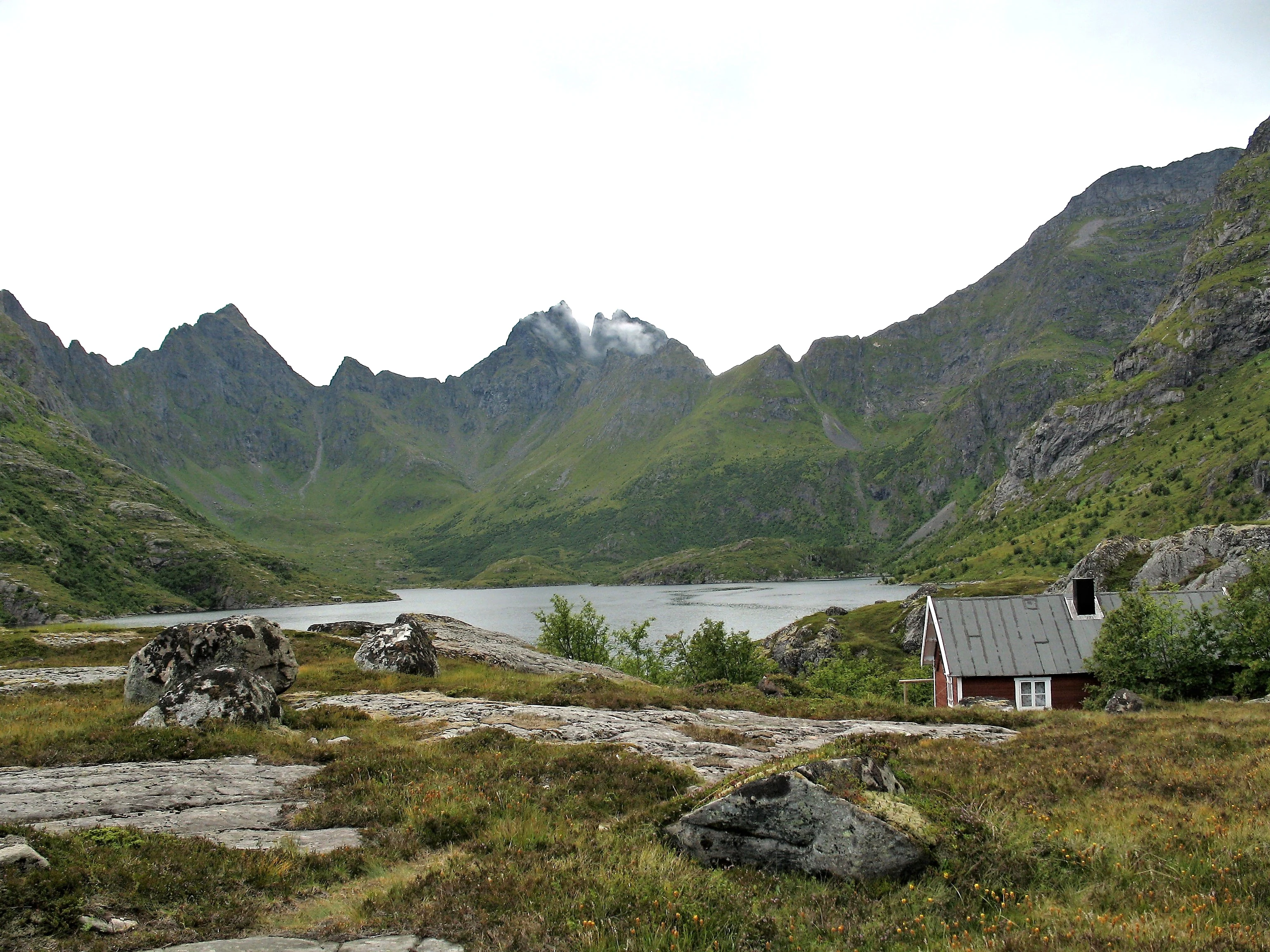 Lake Ågvatnet surrounded by green mountains and rocky terrain, with a small house on the shore