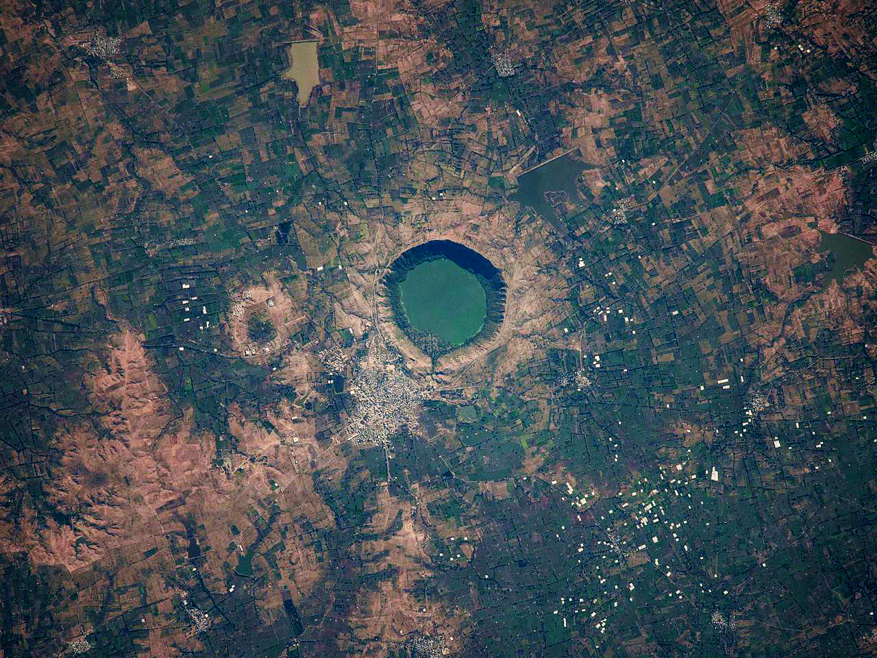 Top-down satellite view of the circular Lonar Lake crater surrounded by agricultural and rural landscape.