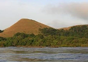 River with calm water in the foreground and a grassy hill with dense vegetation in the background