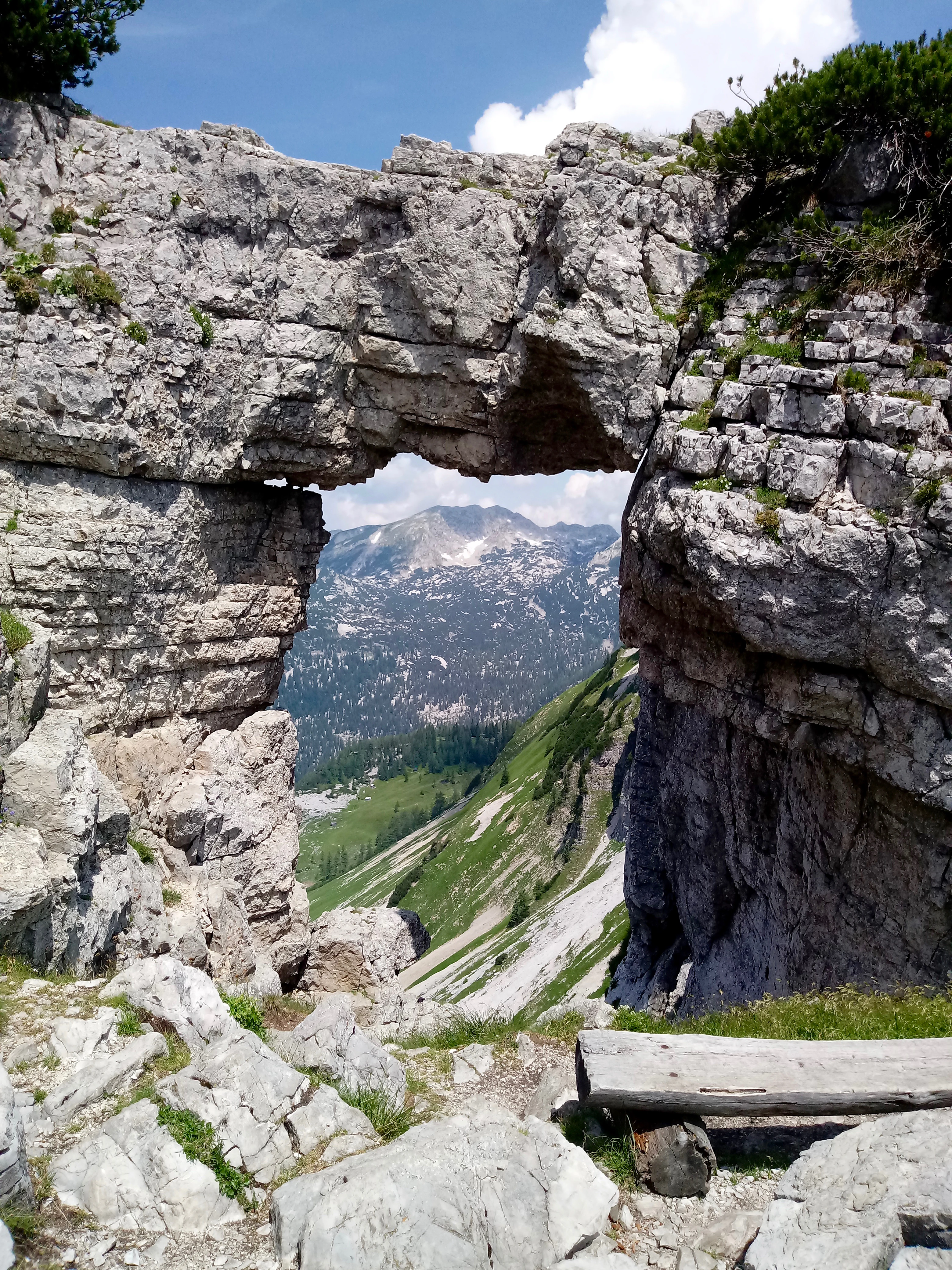 Un gran arco de roca caliza natural que enmarca una vista lejana de laderas verdes y un pico bajo un cielo azul.