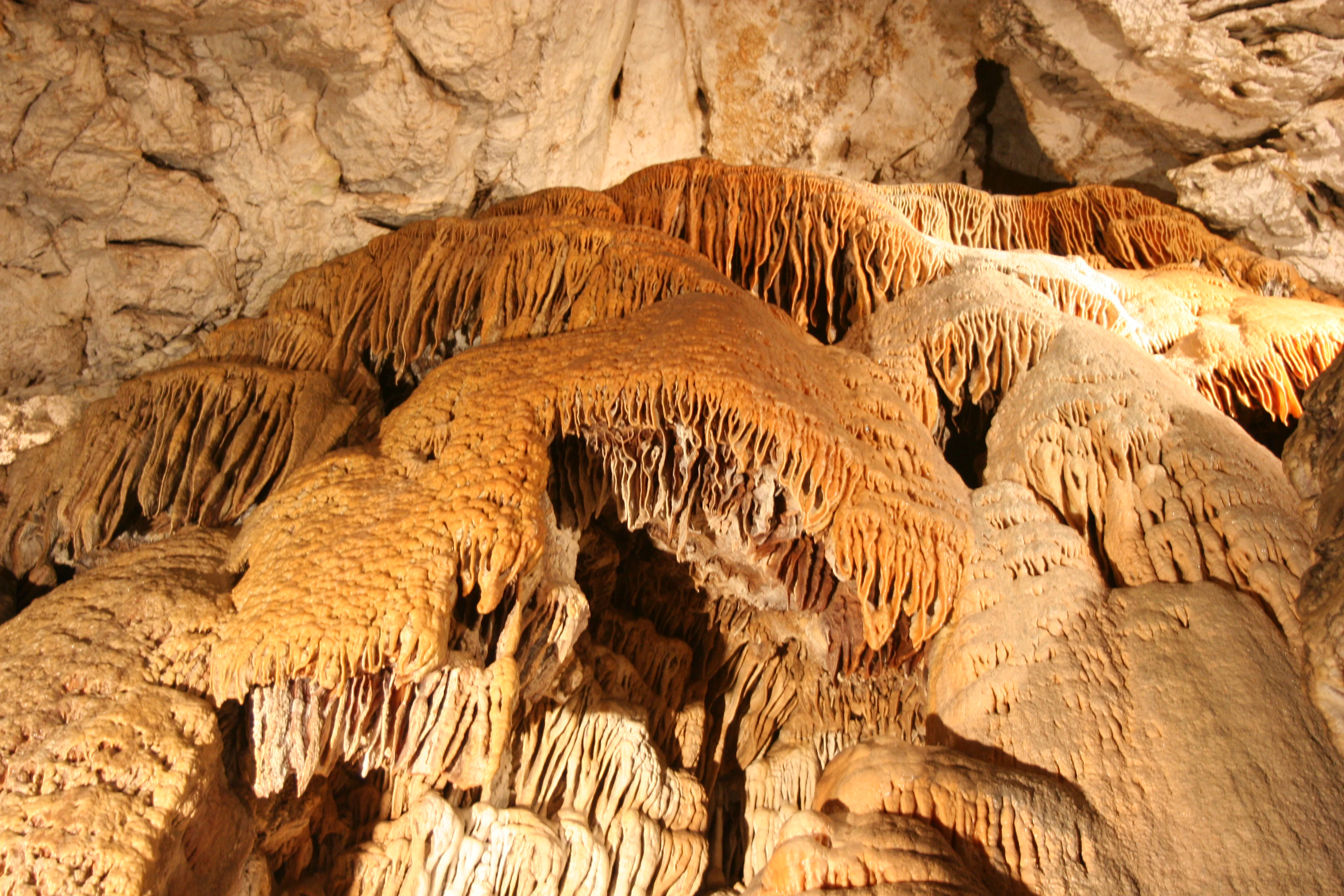 Close-up view of cave formations including stalactites and stalagmites with brown and beige hues