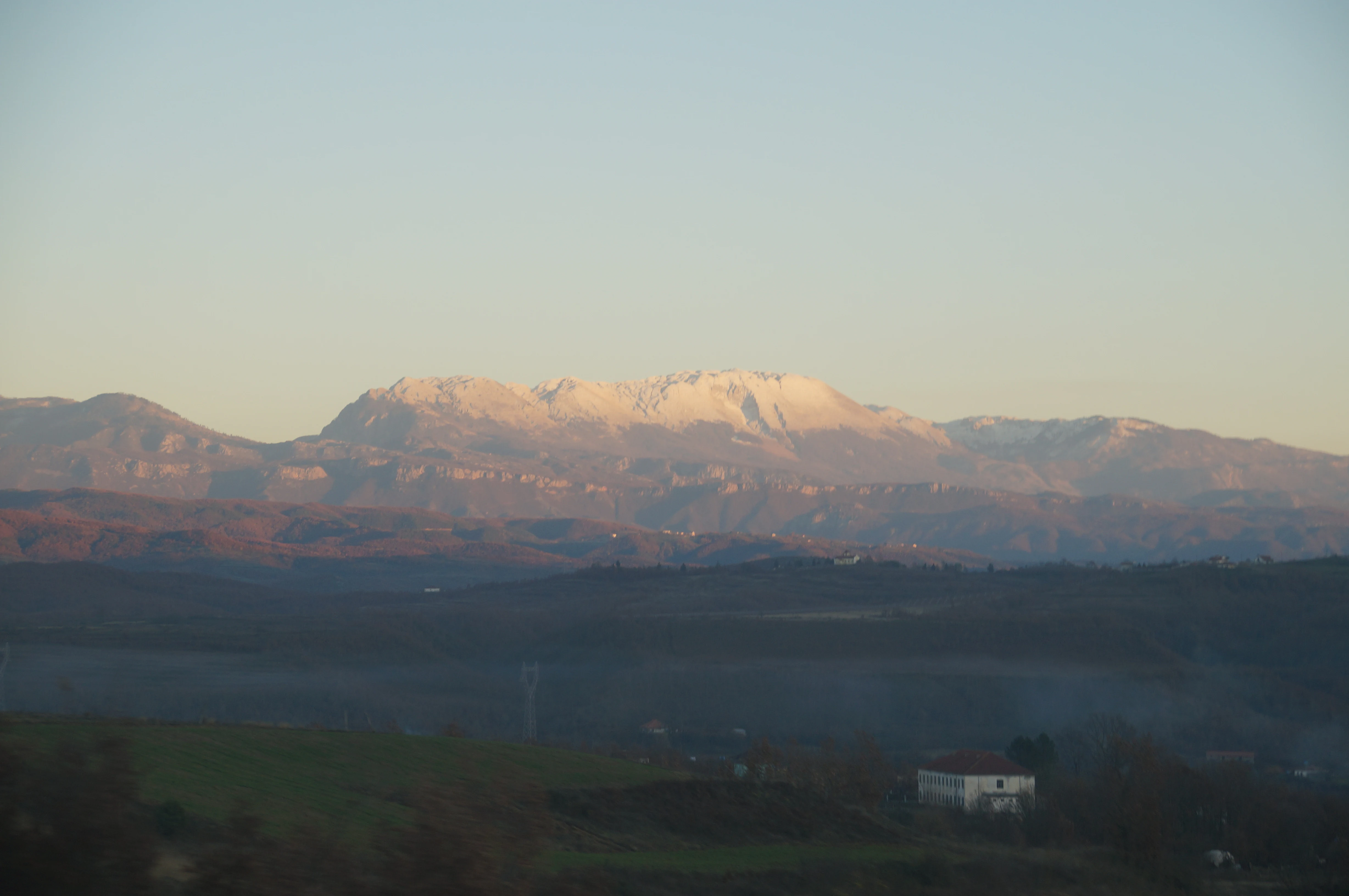 Mountain range with snow-covered peaks, valleys, and a small building in the foreground