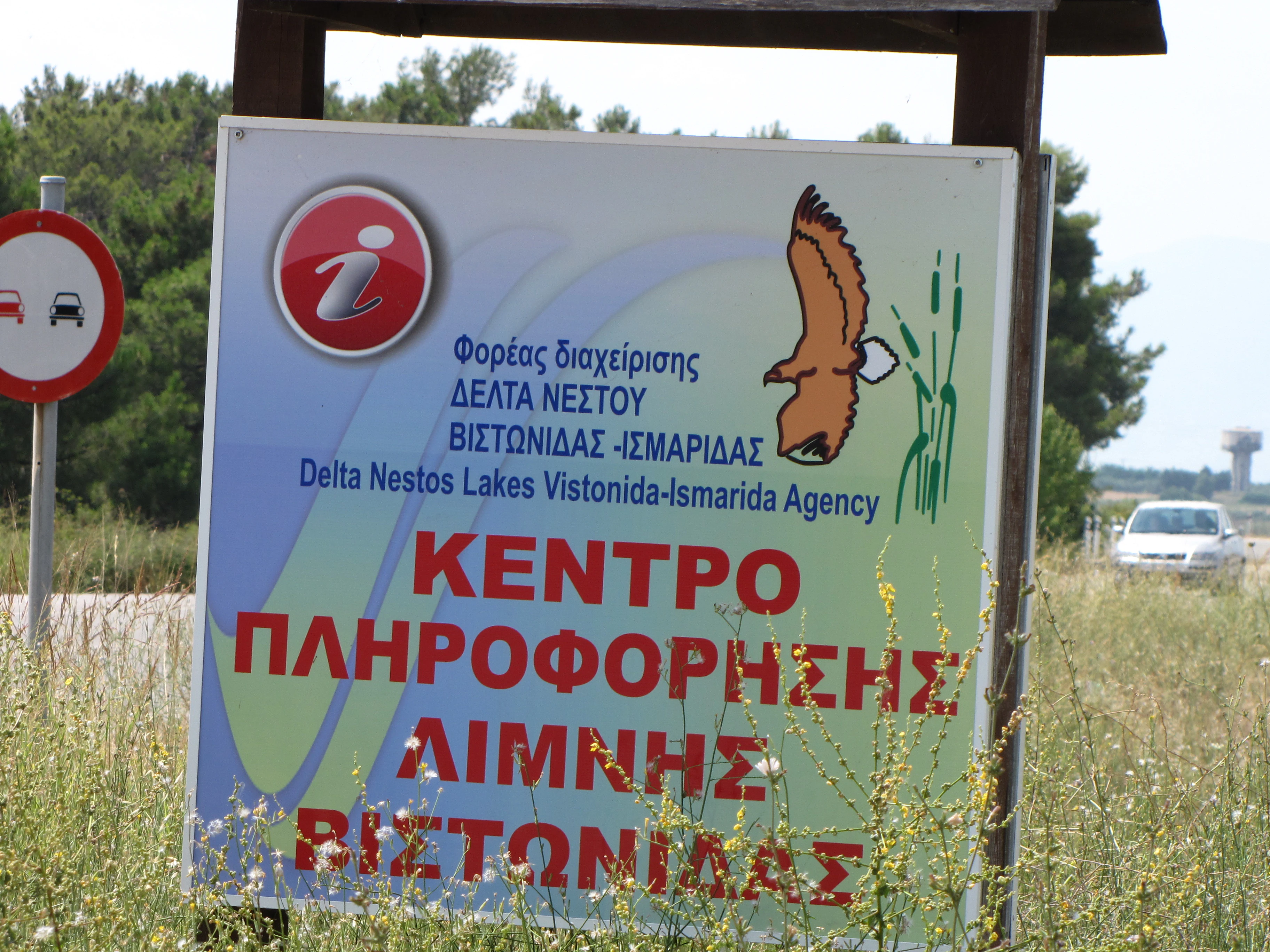 An information sign for the Delta Nestos Lakes Vistonida-Ismarida agency stands outdoors in a grassy area.