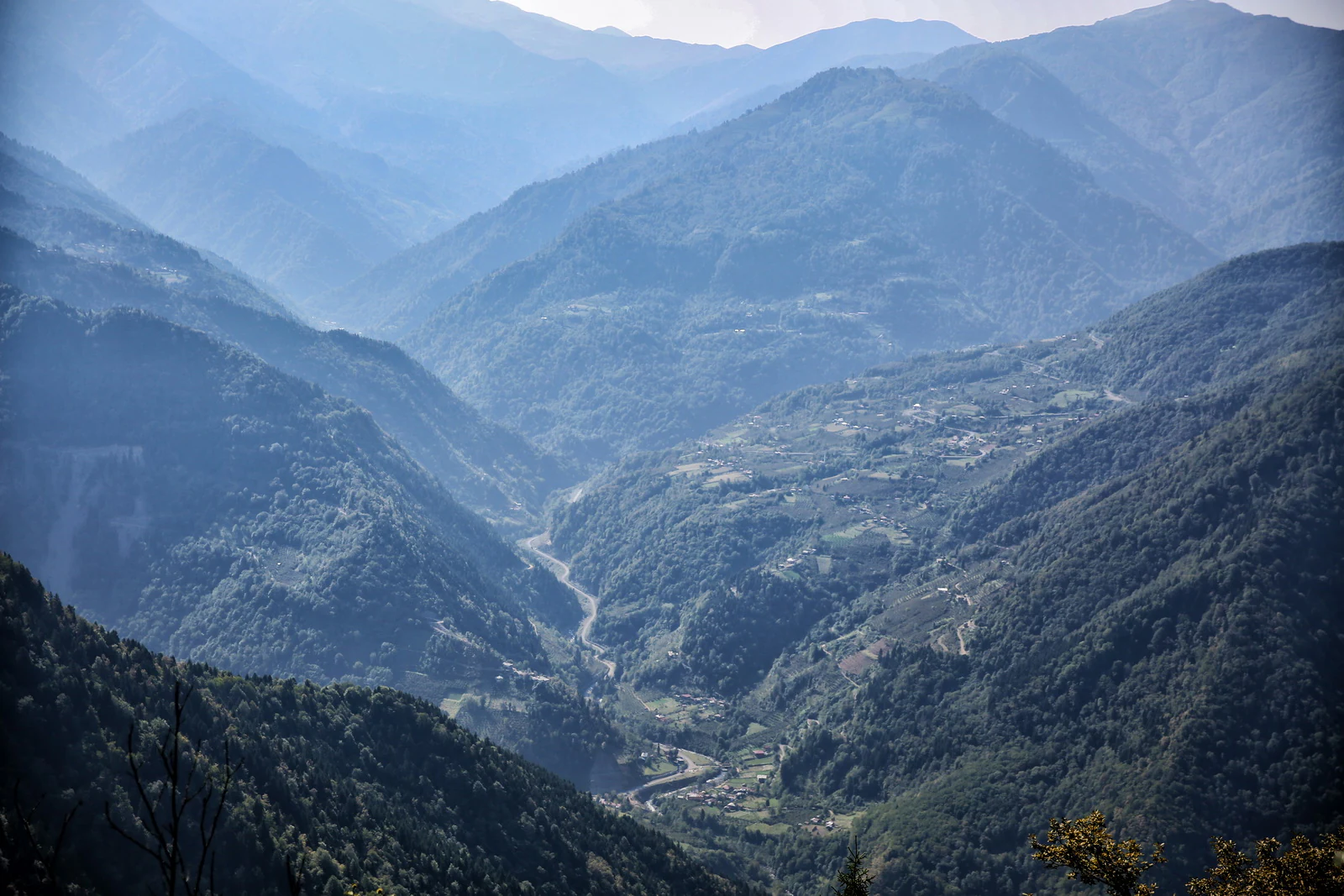 Wide valley view with mountain ranges, forested slopes, and a winding river in the distance