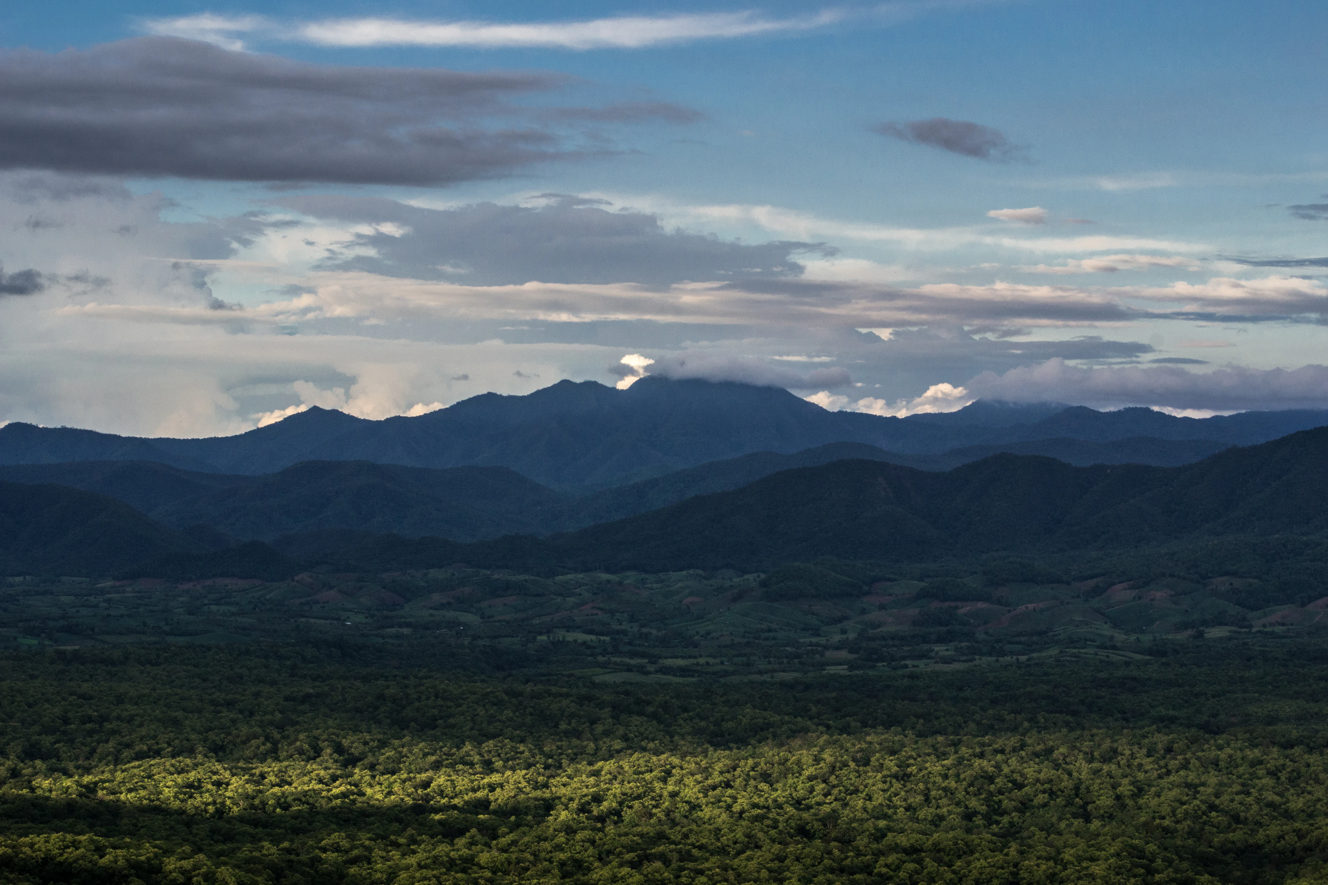 Amplia vista paisajística de una cordillera con un valle boscoso abajo y nubes en el cielo azul