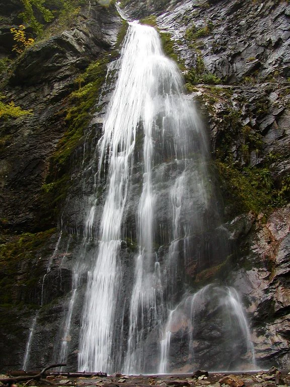 Tall waterfall cascading down a rocky cliff with patches of moss and vegetation