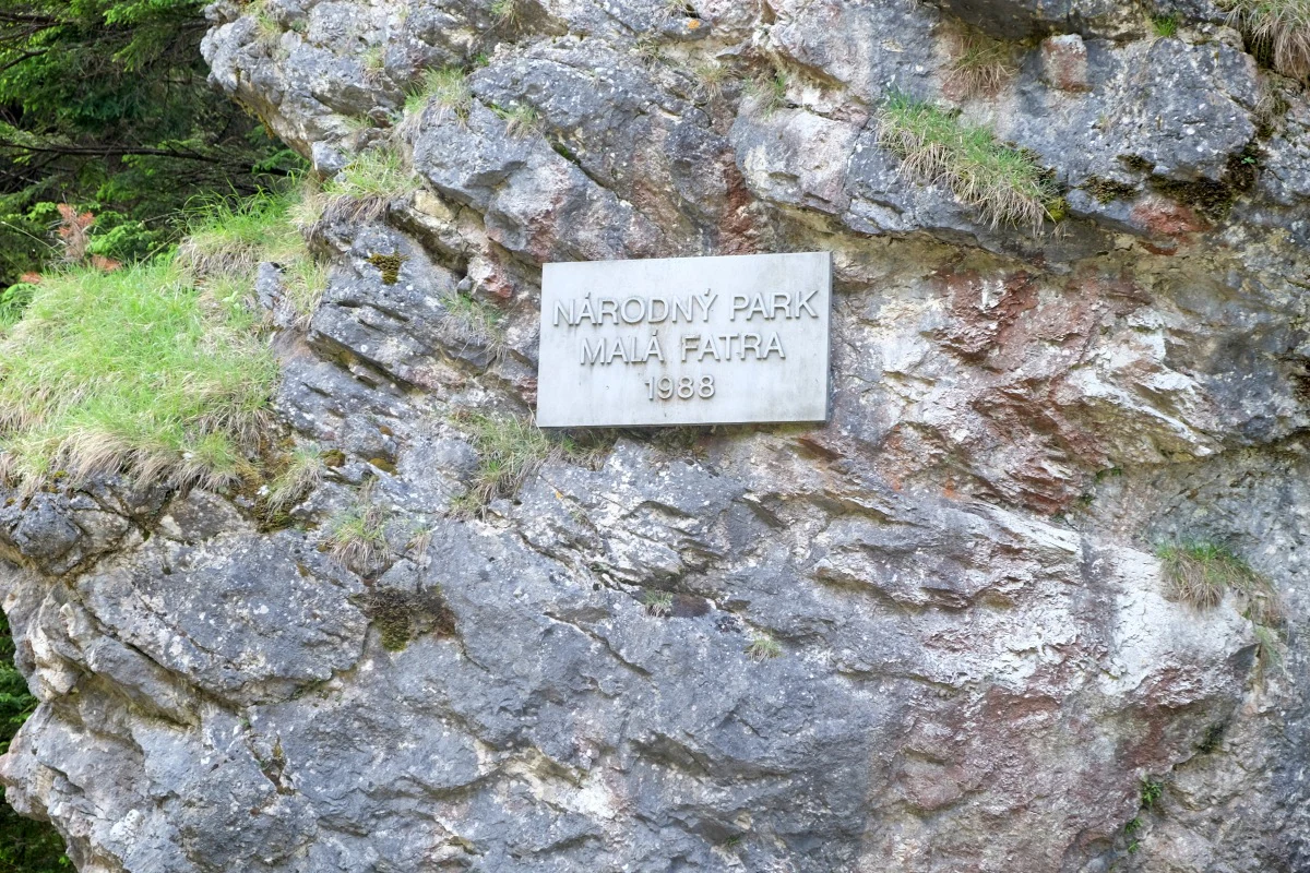 Stone sign reading 'NÁRODNÝ PARK MALÁ FATRA 1988' mounted on a rocky cliff face with patches of grass