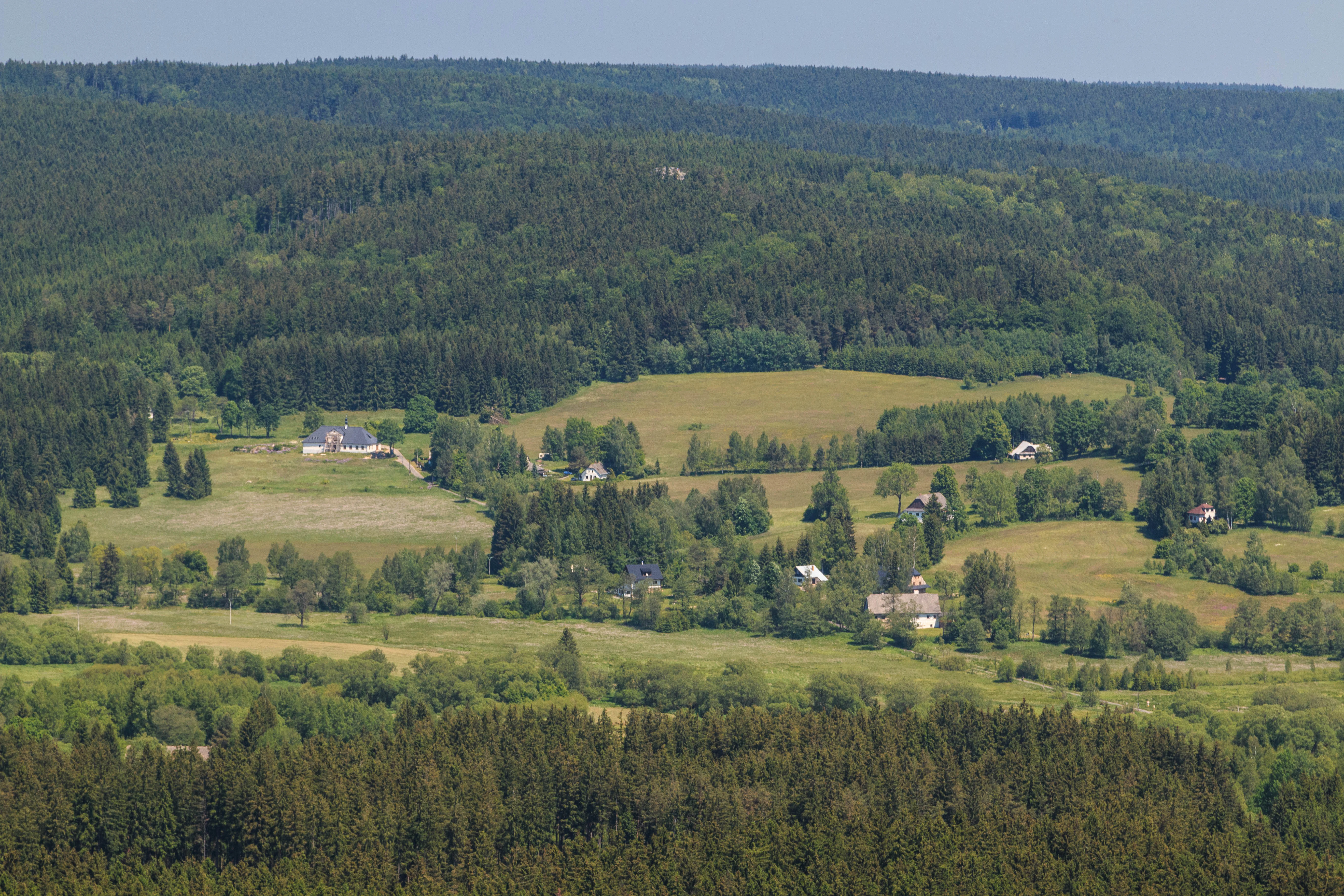 Una vista en ángulo alto sobre un mosaico de prados verdes, pequeñas casas de campo y densos bosques de coníferas en el campo checo.