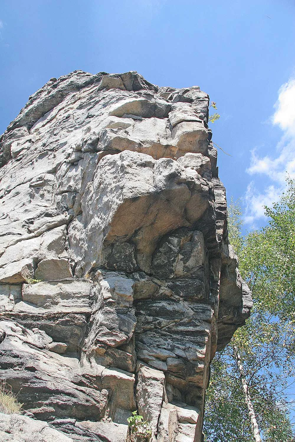 Una vista a baja altura de la escarpada formación rocosa de Malinska skala contra un cielo azul despejado con algunos árboles verdes a la derecha.
