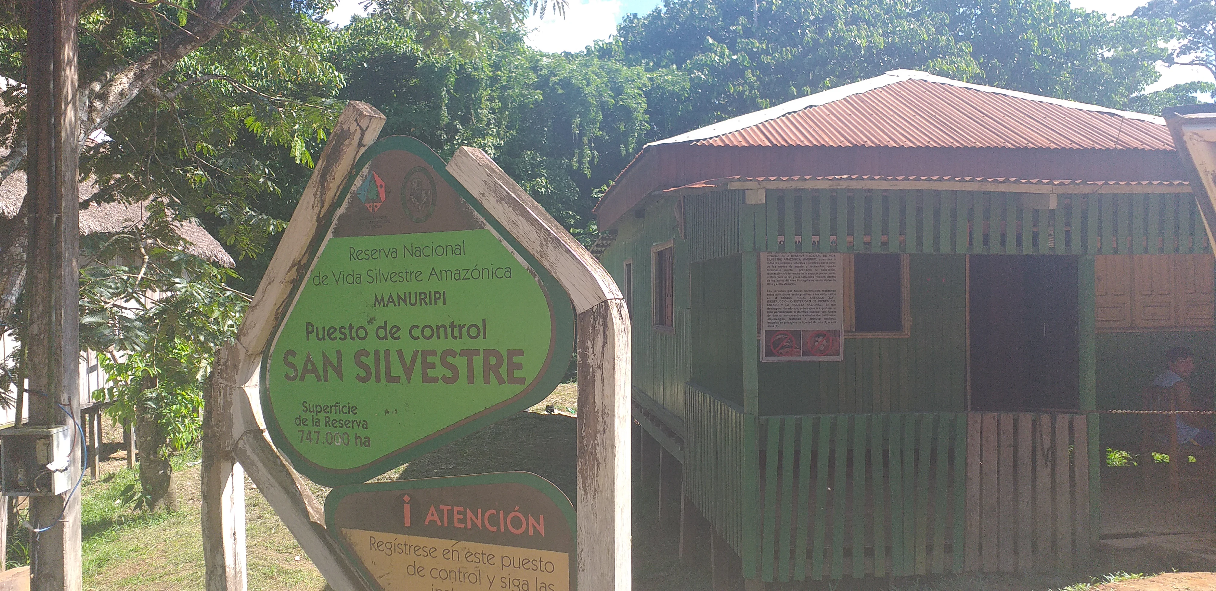 A green sign with white text reading San Silvestre control station stands in front of a wooden structure in a forested area.