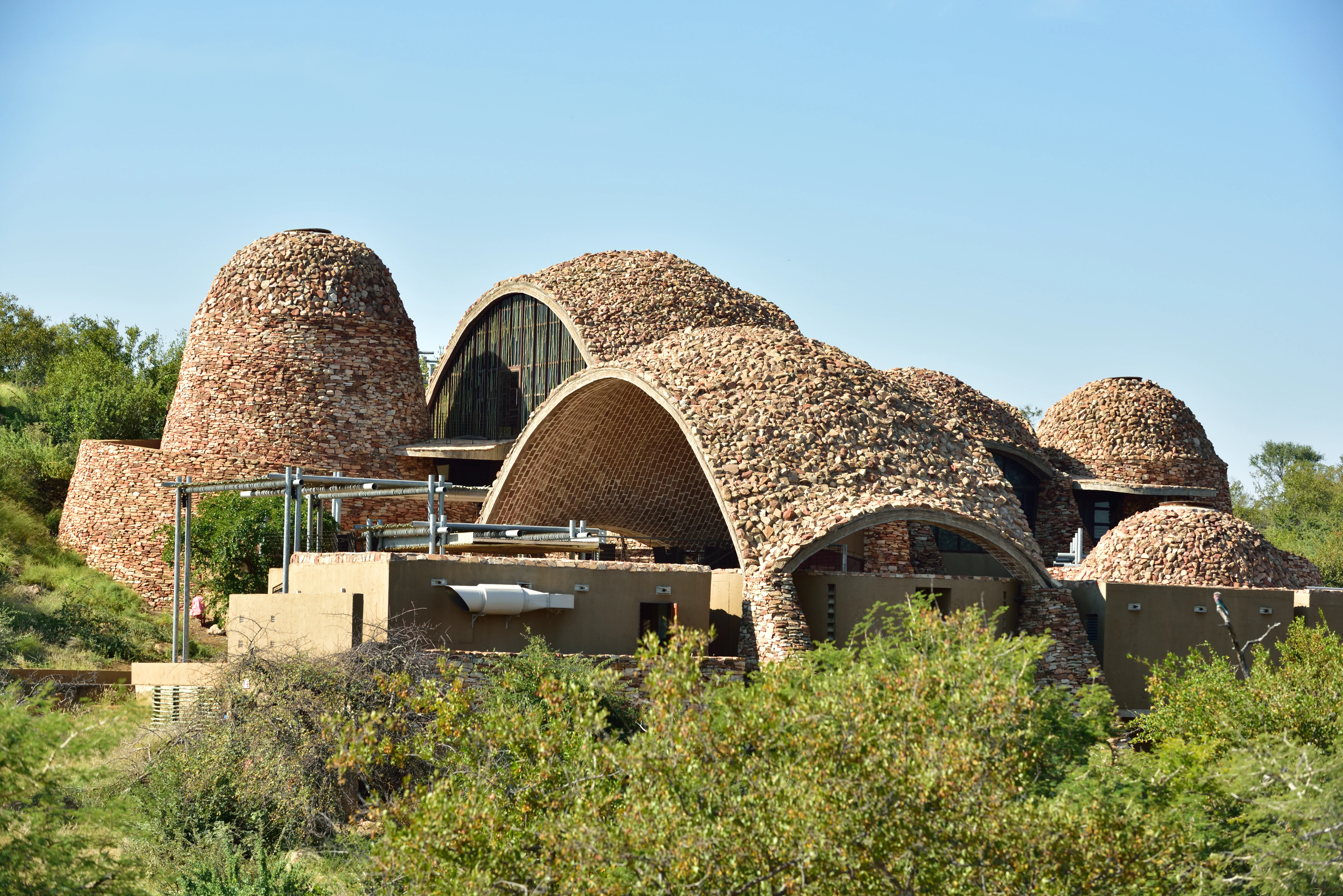 Edificios con cúpulas de piedra con estructuras arqueadas rodeados de vegetación verde bajo un cielo azul despejado