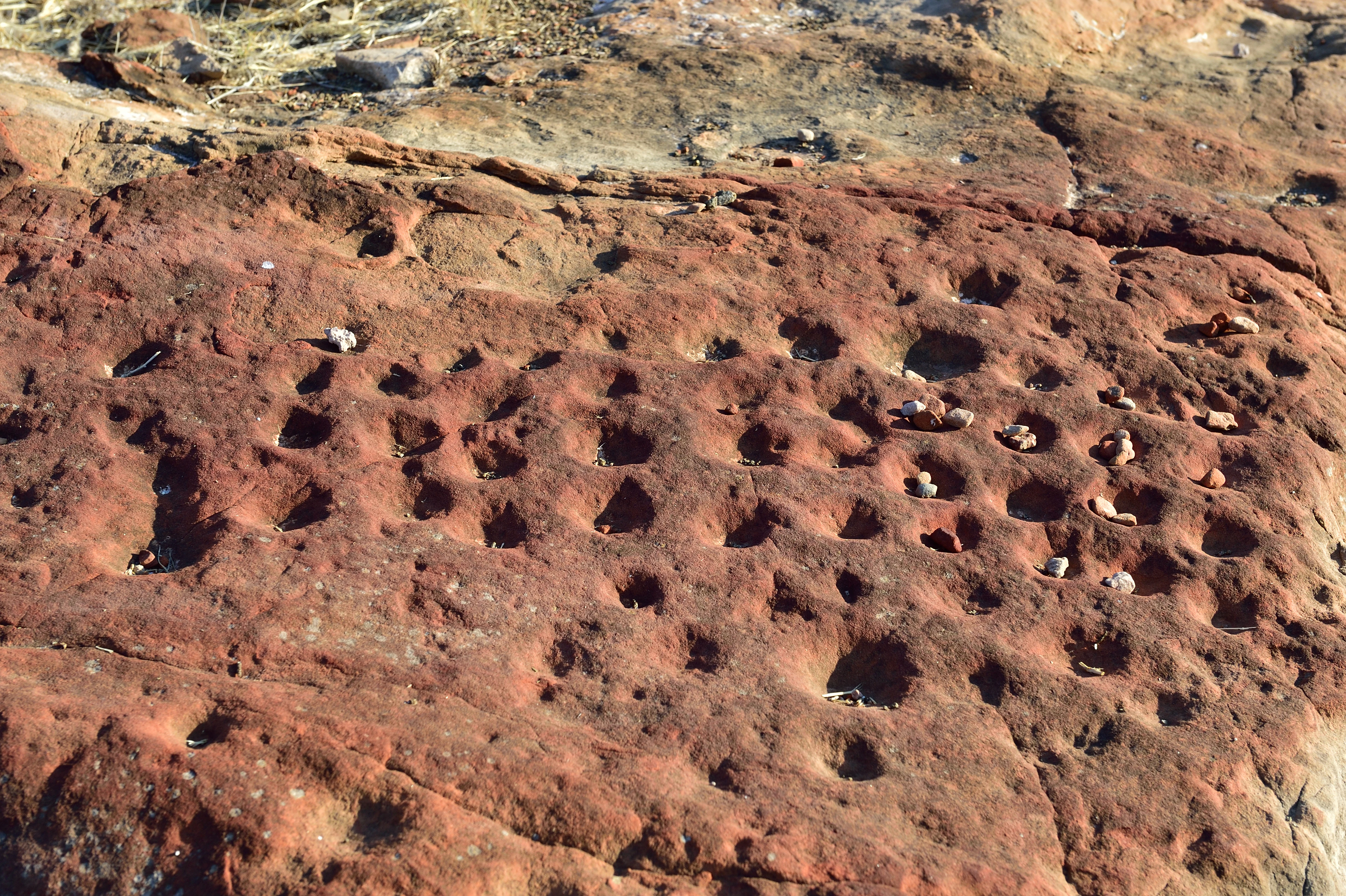 Primer plano de un tablero de juego de piedra con múltiples hendiduras circulares talladas en una superficie de roca de color marrón rojizo