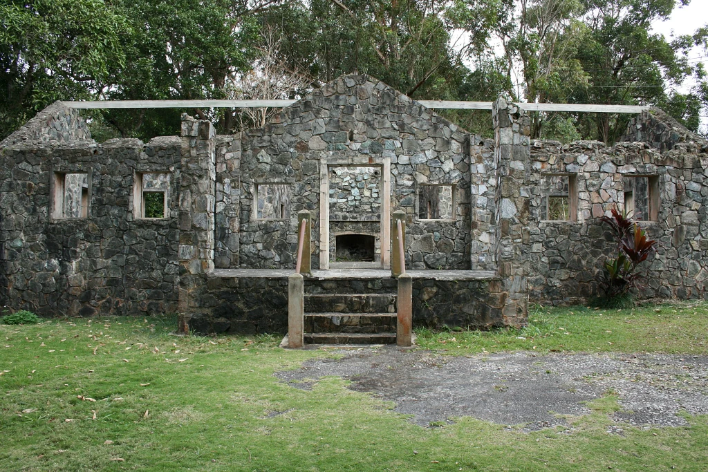 Una estructura parcial de piedra conocida como Casa de Piedra, con muros y una entrada central, frente a un fondo de bosque verde.