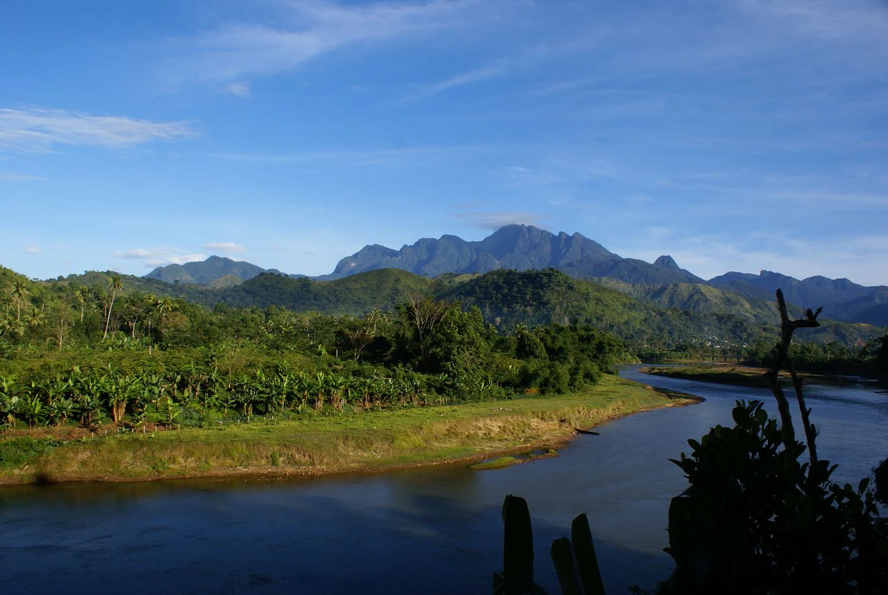 River flowing through lush green valley with mountain ranges in background under clear blue sky