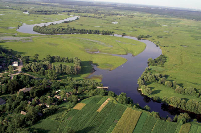 Aerial view of a winding river through green fields and forests with scattered buildings in Mezyn National Nature Park