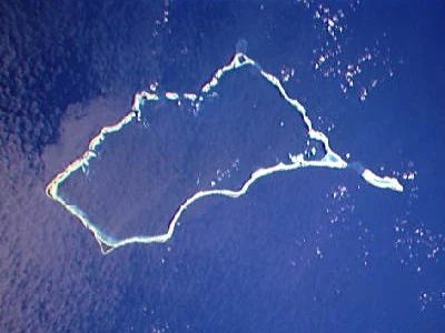 Aerial satellite photograph of Mili Atoll, a coral atoll forming an irregular ring shape with light turquoise and white reef edges surrounded by deep blue ocean water