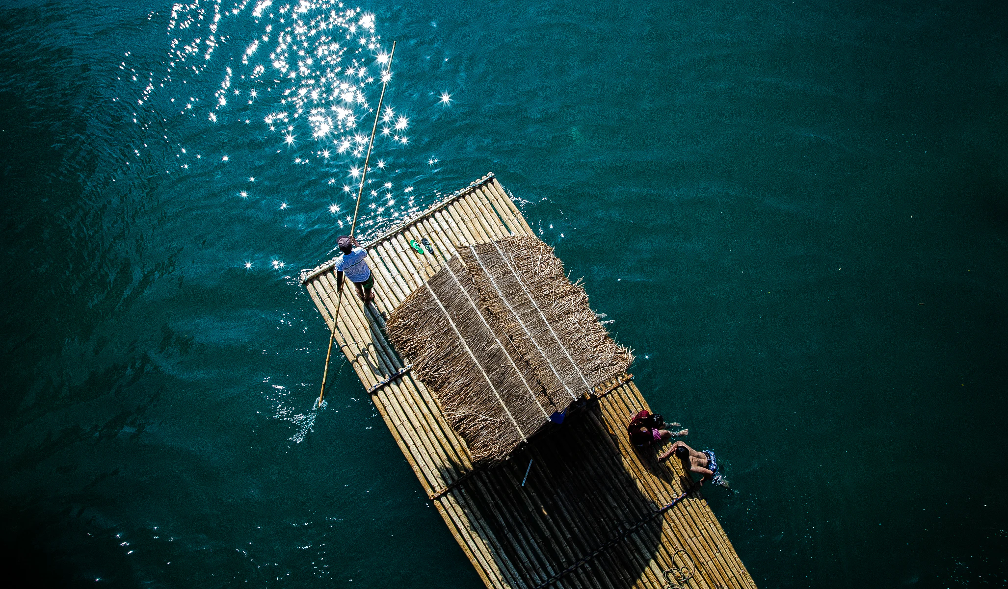 Aerial view of a bamboo raft with two people navigating the river using a pole