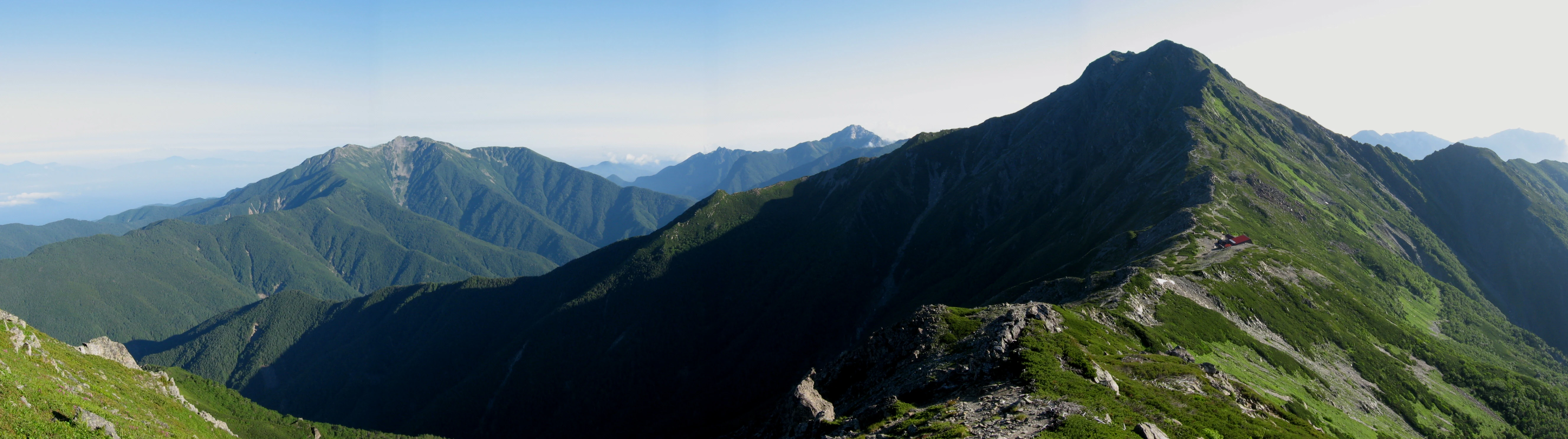 Panoramic view of mountain ranges with green slopes and rocky peaks under a clear blue sky