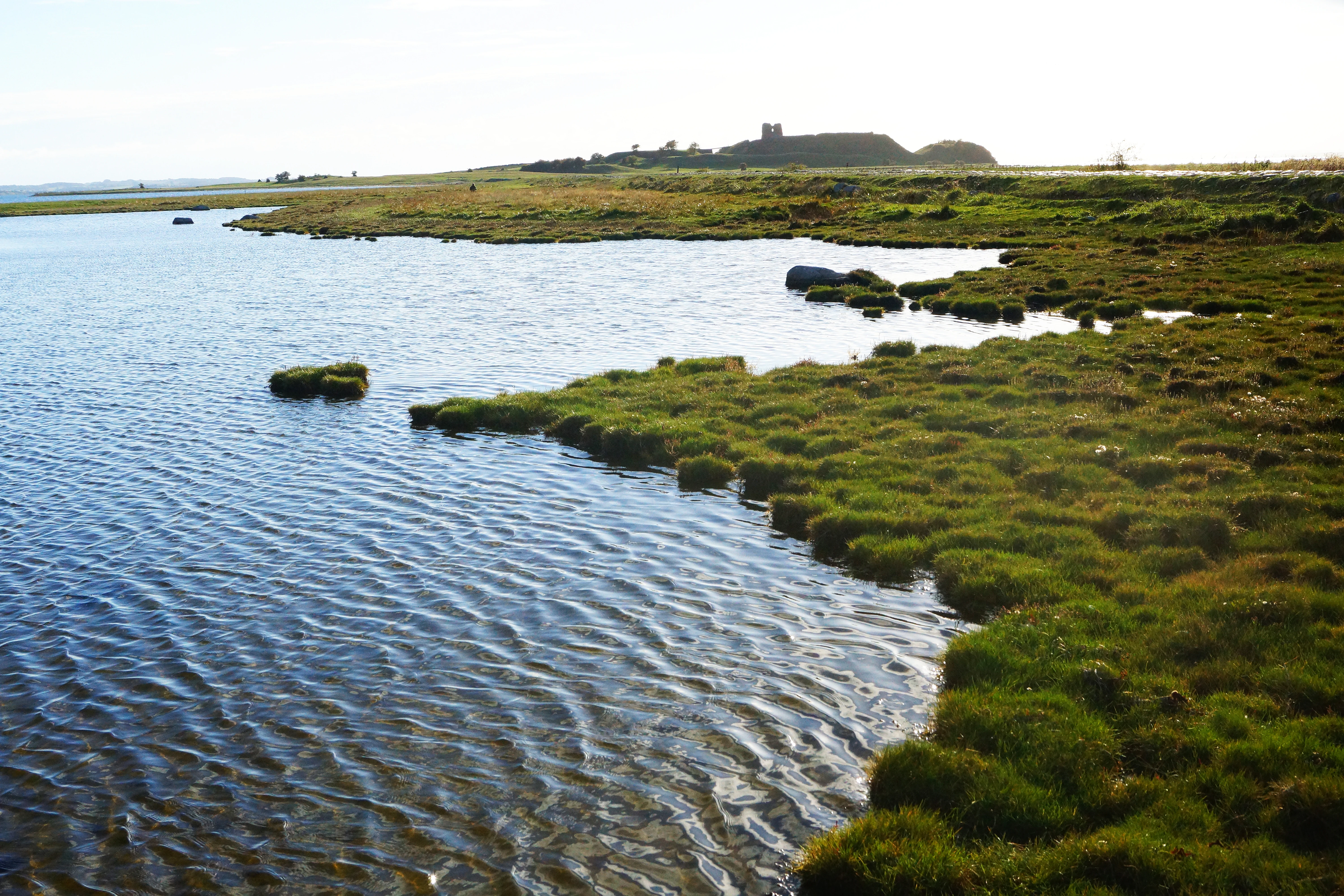 Water with grassy shoreline and distant ruin structure visible on the horizon