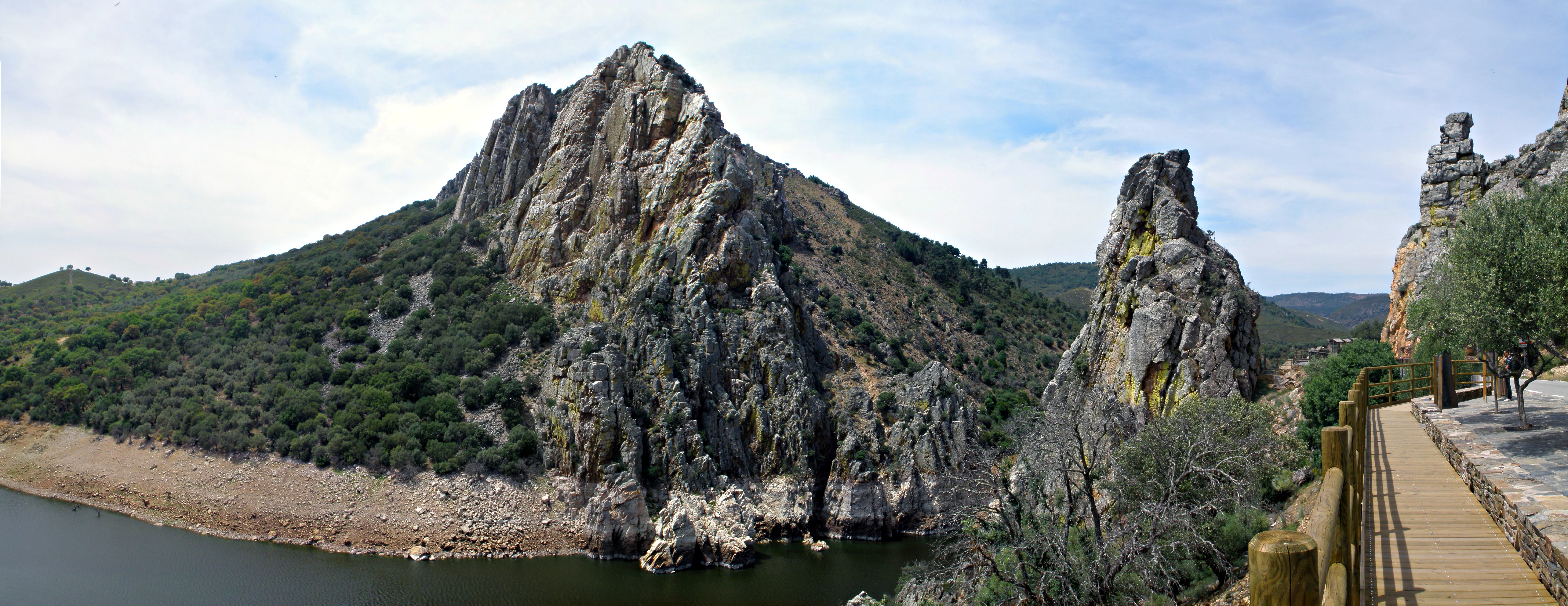 Panoramic view of Salto del Gitano cliff face with a wooden walkway, body of water, and rocky terrain surrounded by vegetation