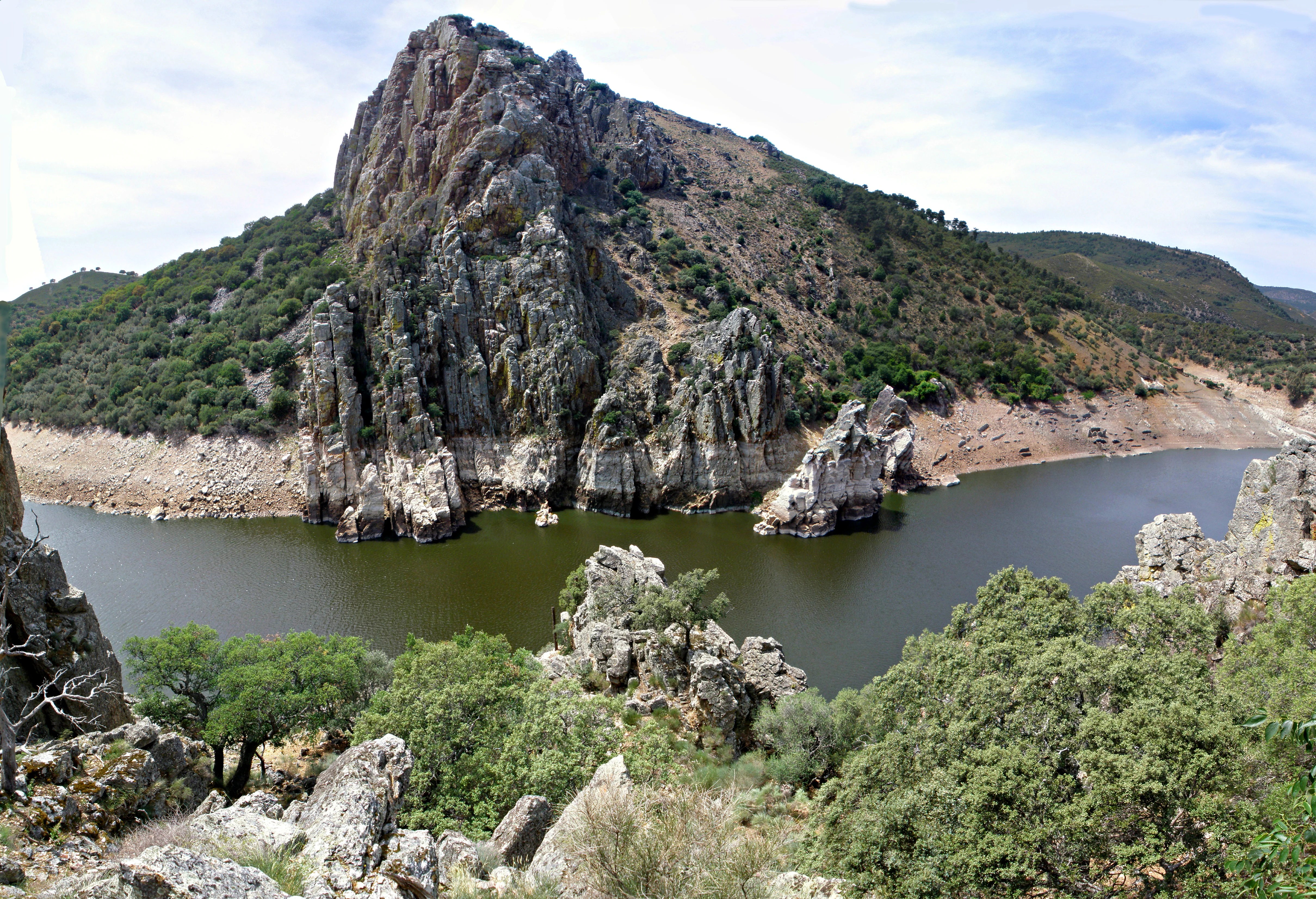 Large rocky cliff formation beside a calm water reservoir with green vegetation in the foreground