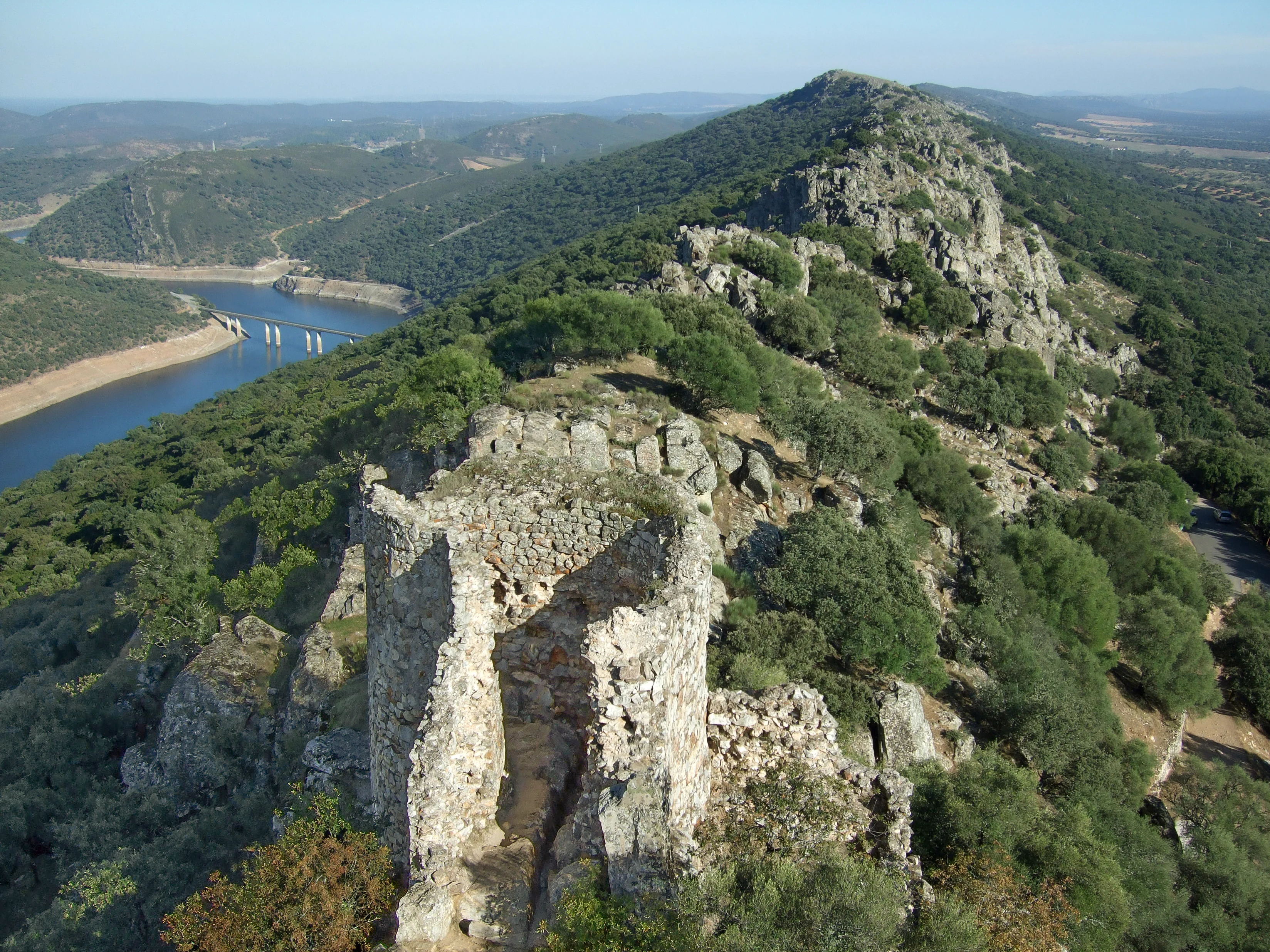 Ruins of Monfragüe Castle overlooking the Tajo River with forested hills and rocky terrain