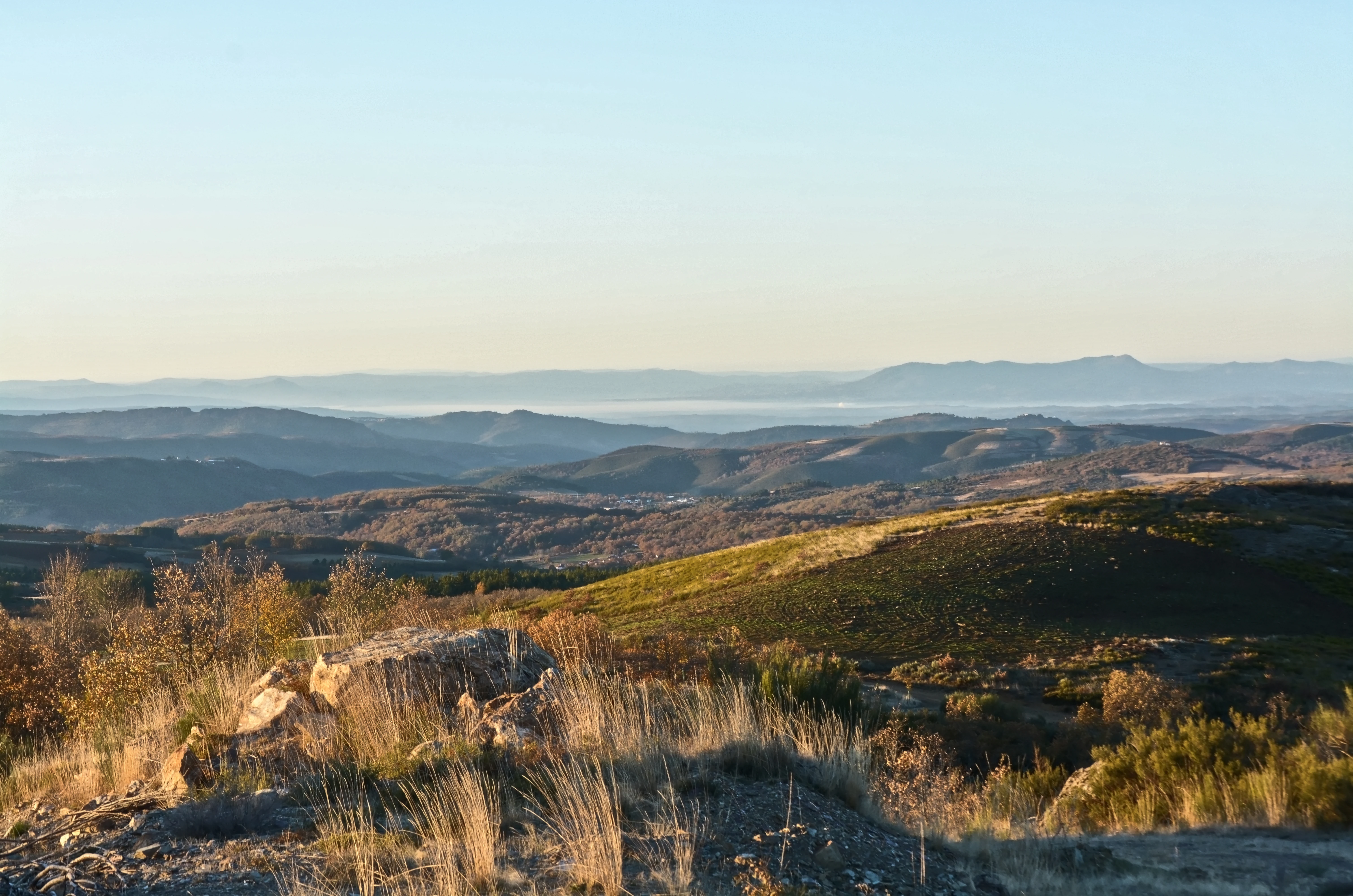 Wide landscape view of Montesinho Natural Park featuring rolling hills, sparse vegetation, and distant mountain ranges under a clear sky
