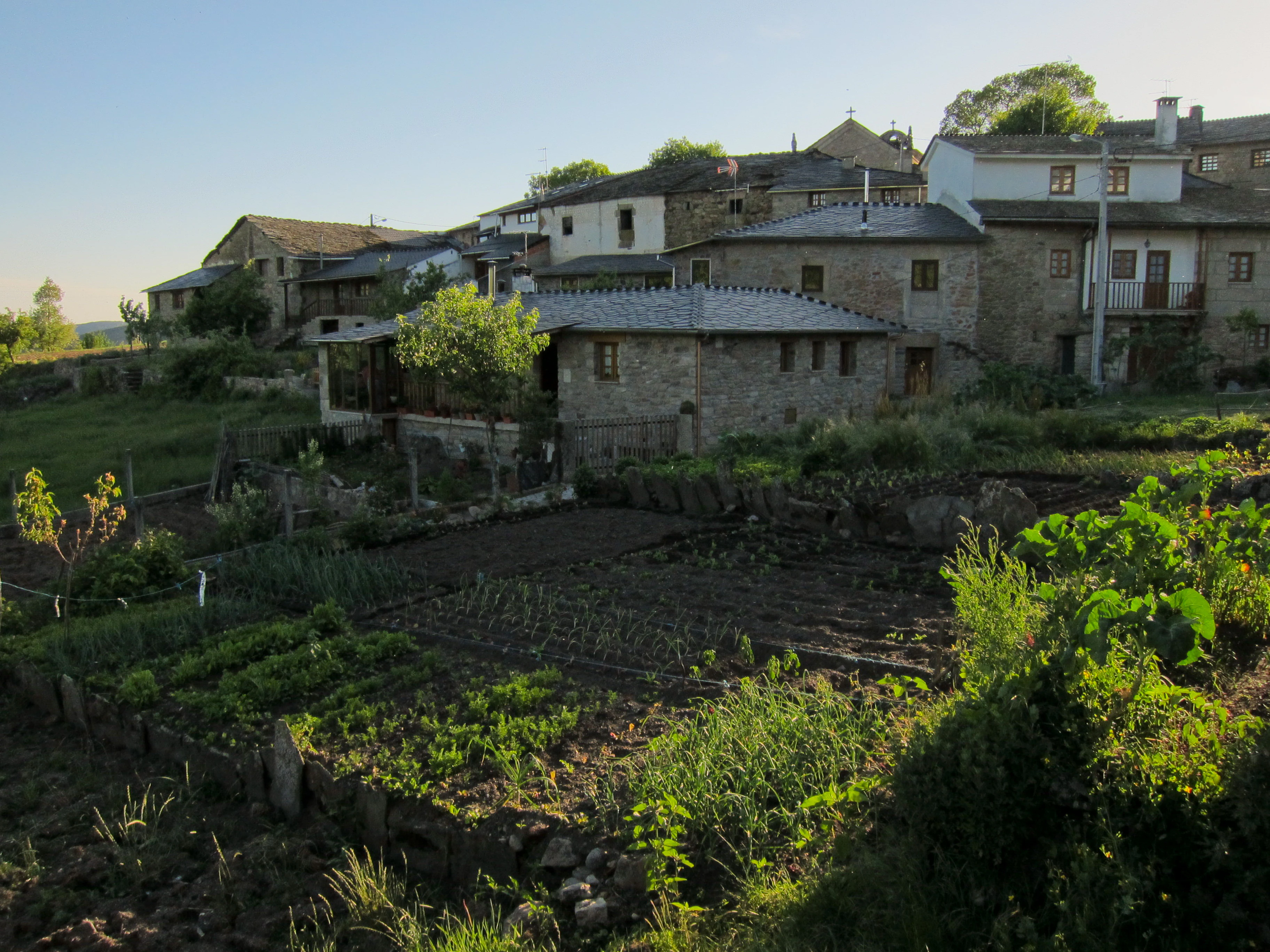 Stone houses and agricultural fields in a rural village landscape with greenery and hills in the background