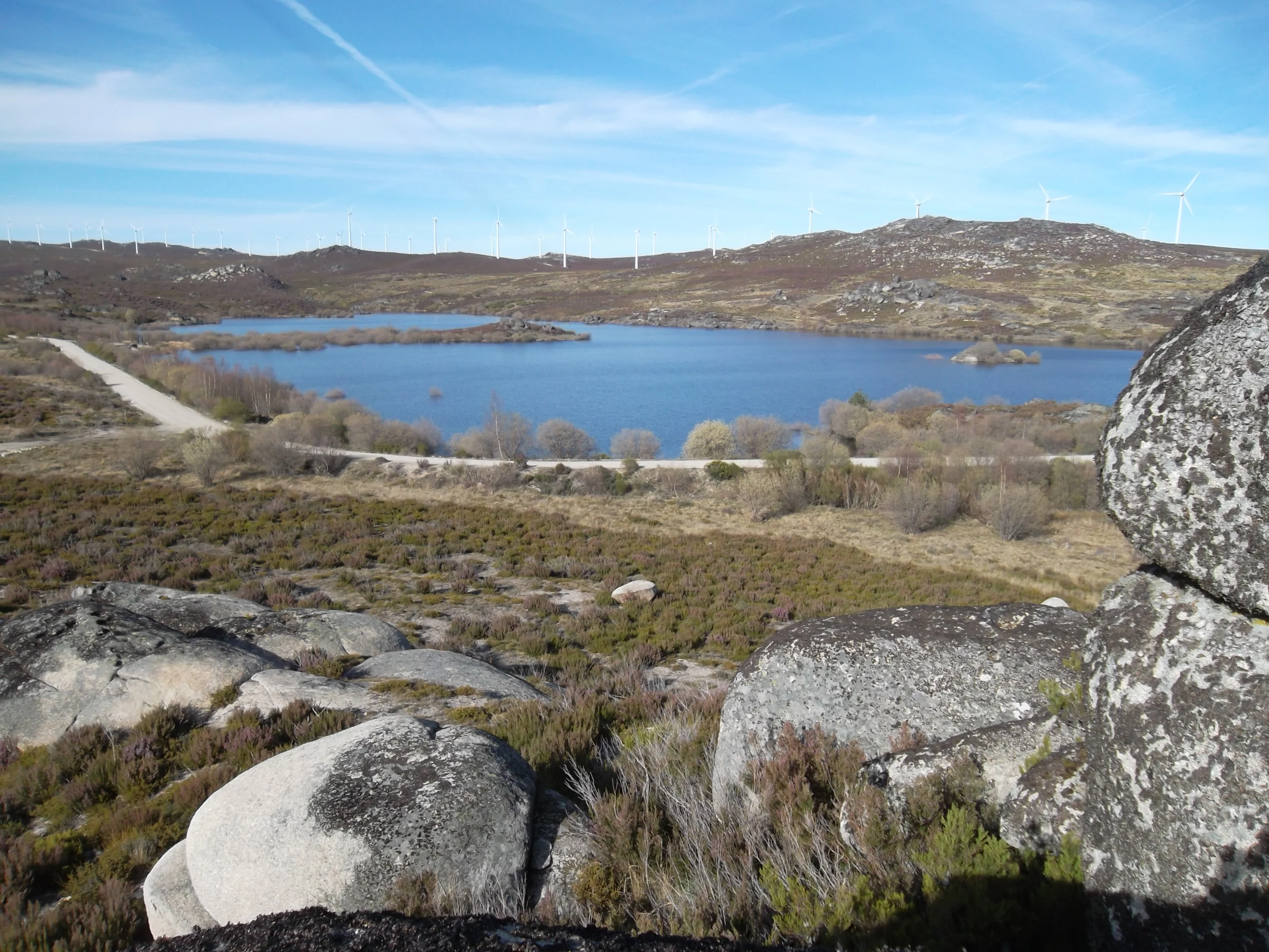Wide landscape view of Serra Serrada Reservoir with rocky foreground, calm blue water, distant hills, and clear sky.