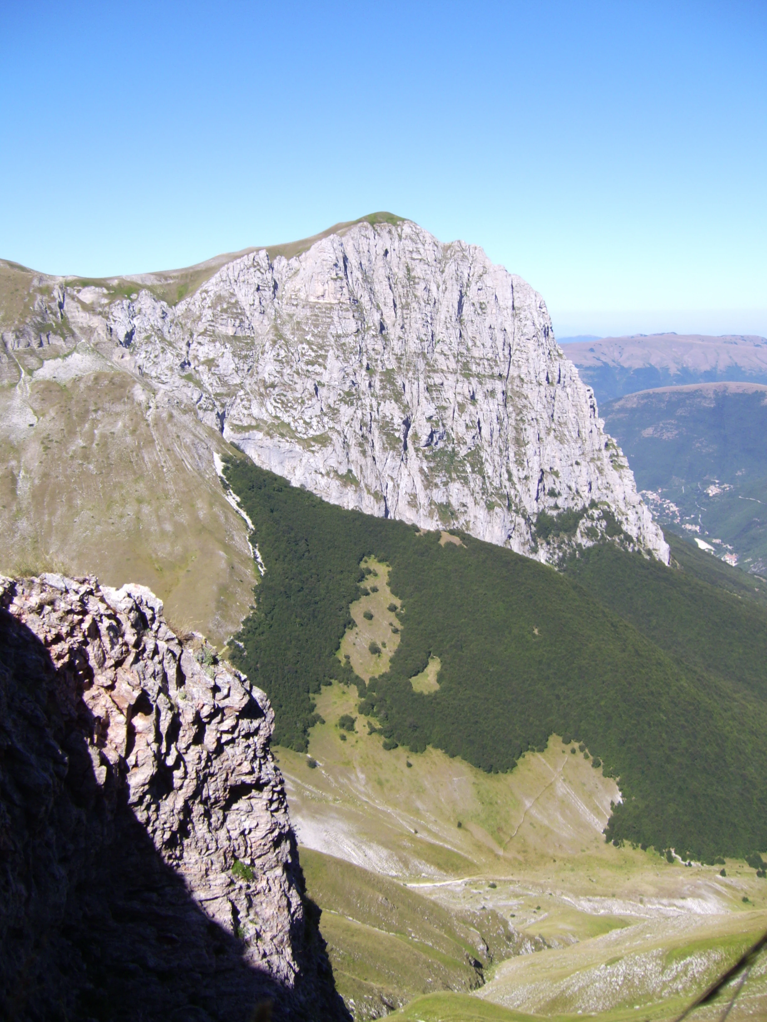 Rocky mountain peak with steep cliffs and green valleys under clear blue sky