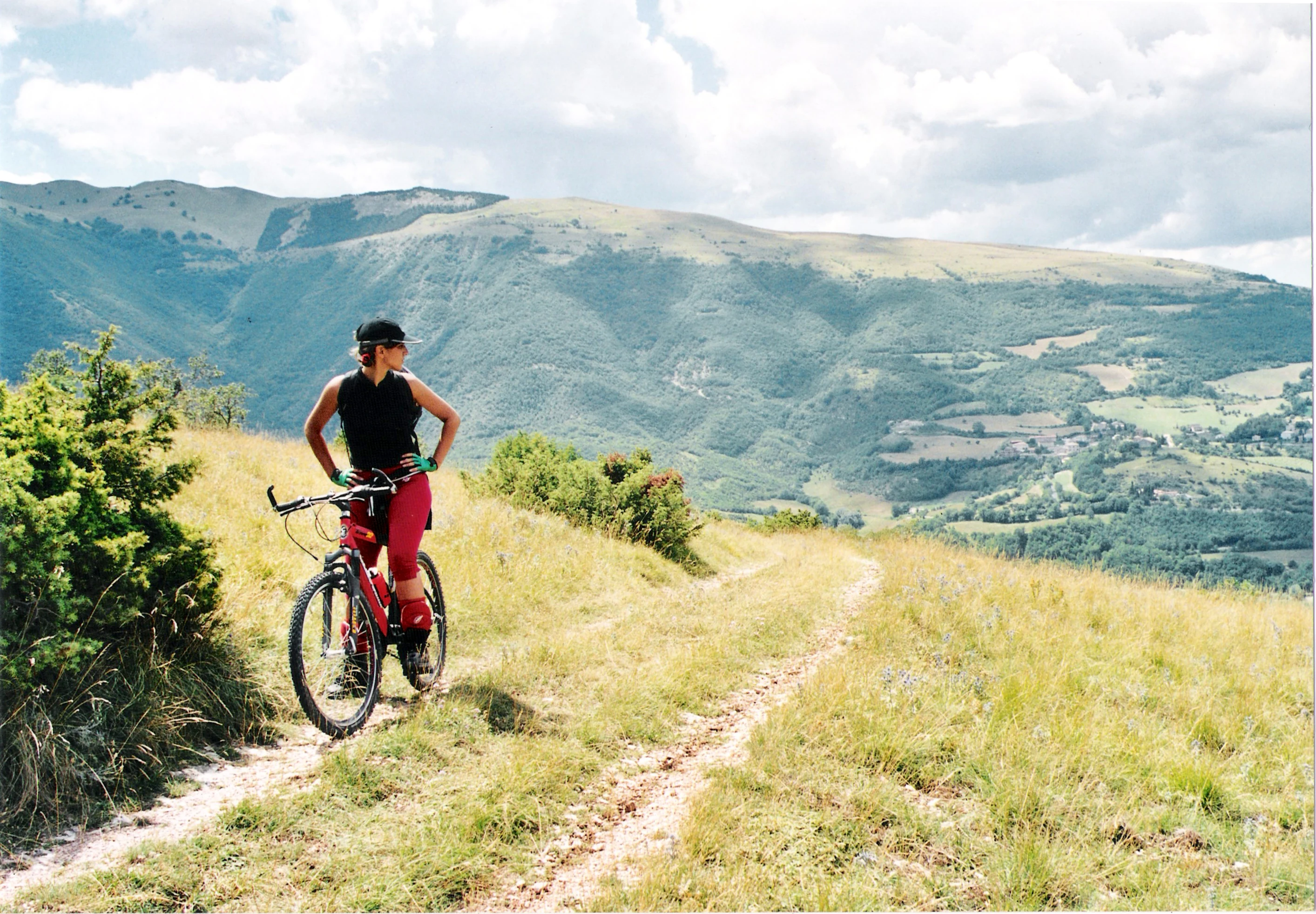 A person riding a mountain bike on a grassy trail with mountainous landscape in the background