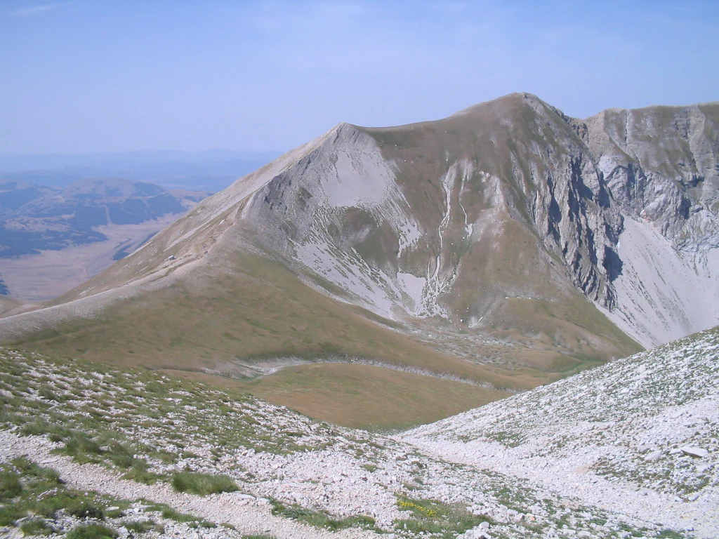 Mountain peak with rocky slopes and grassy terrain under a clear blue sky