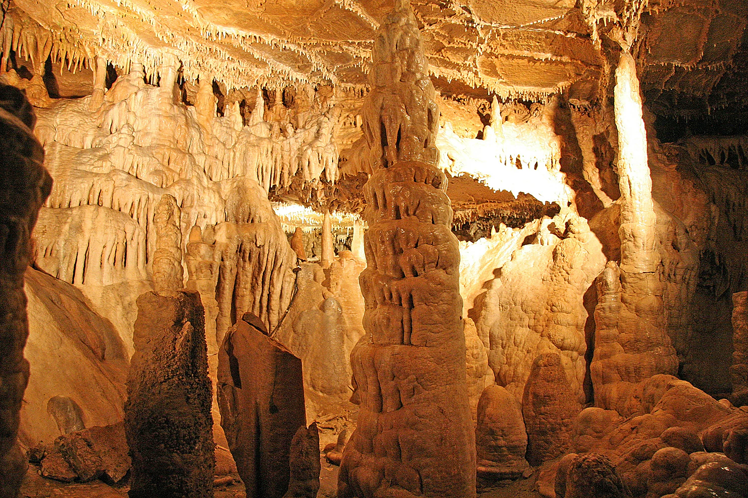 Cave interior with stalactites hanging from ceiling and stalagmites rising from floor, illuminated by artificial lighting