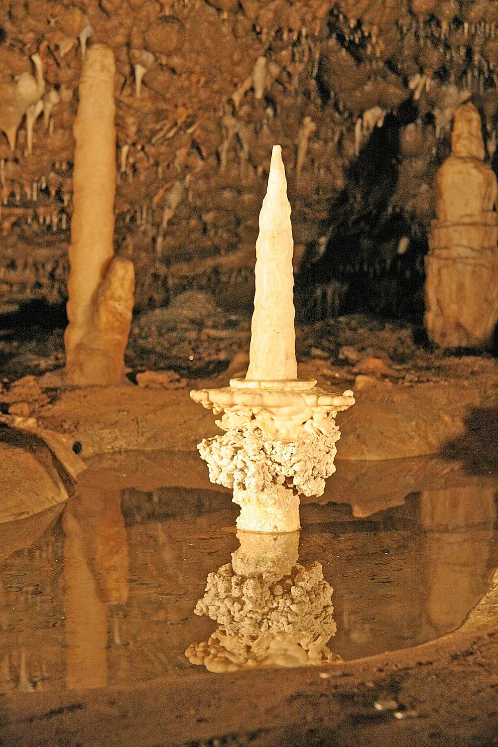 Stalagmite formation named 'Candle' with reflection in water inside a cave, surrounded by other rock formations