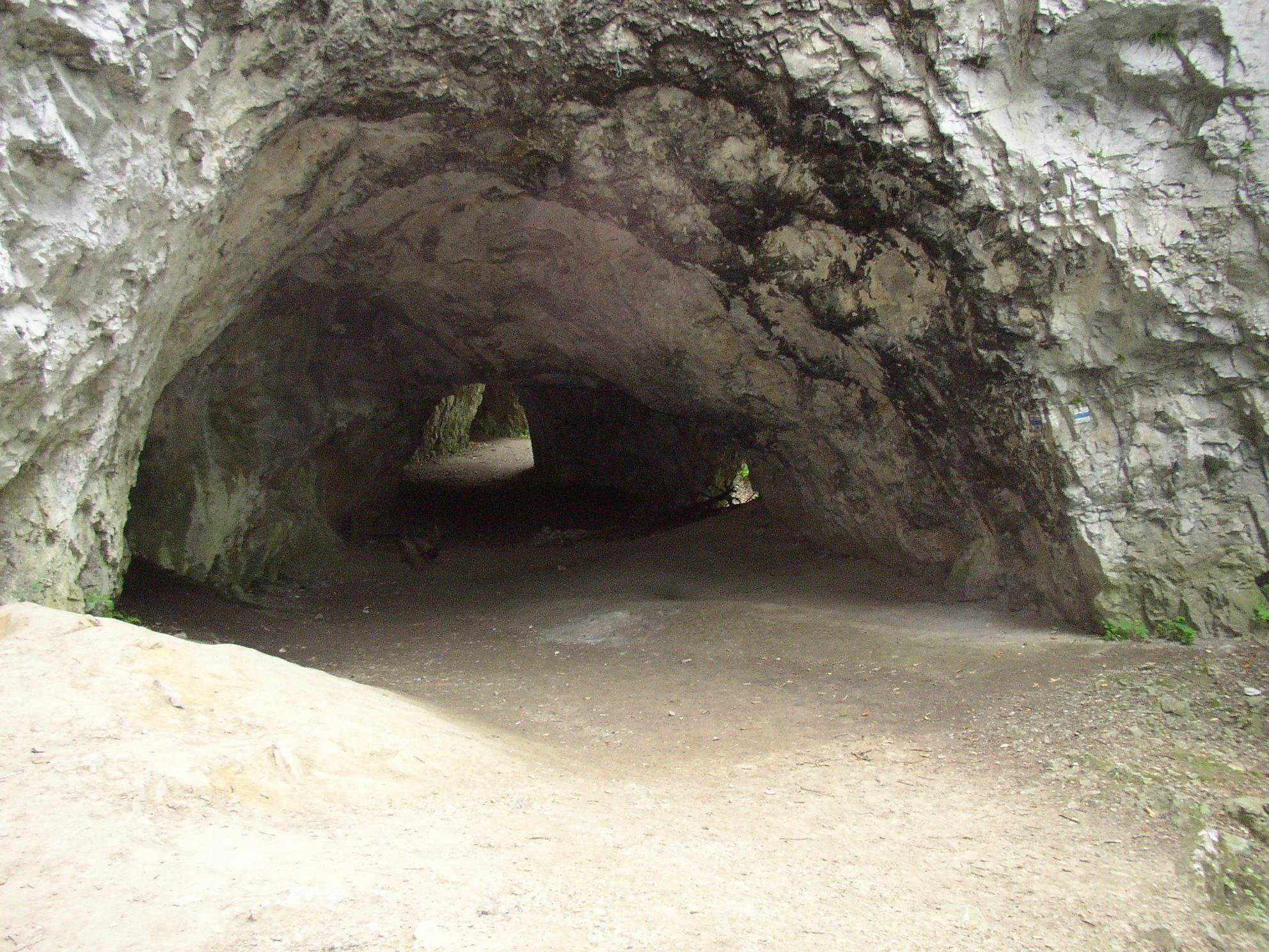 Rocky cave entrance with a dirt path leading into a dark interior, surrounded by rugged stone walls
